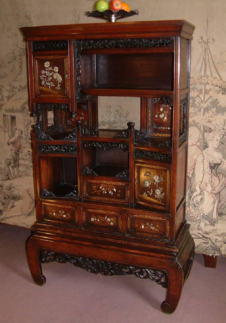 A small Japanese hardwood Meiji period Shibayama inlaid cabinet (shodana) dating from circa 1870. The planked top above an asymmetrical assortment of open shelves, two cupboards and four drawers with detailed carved Ivory, mother-of-pearl and