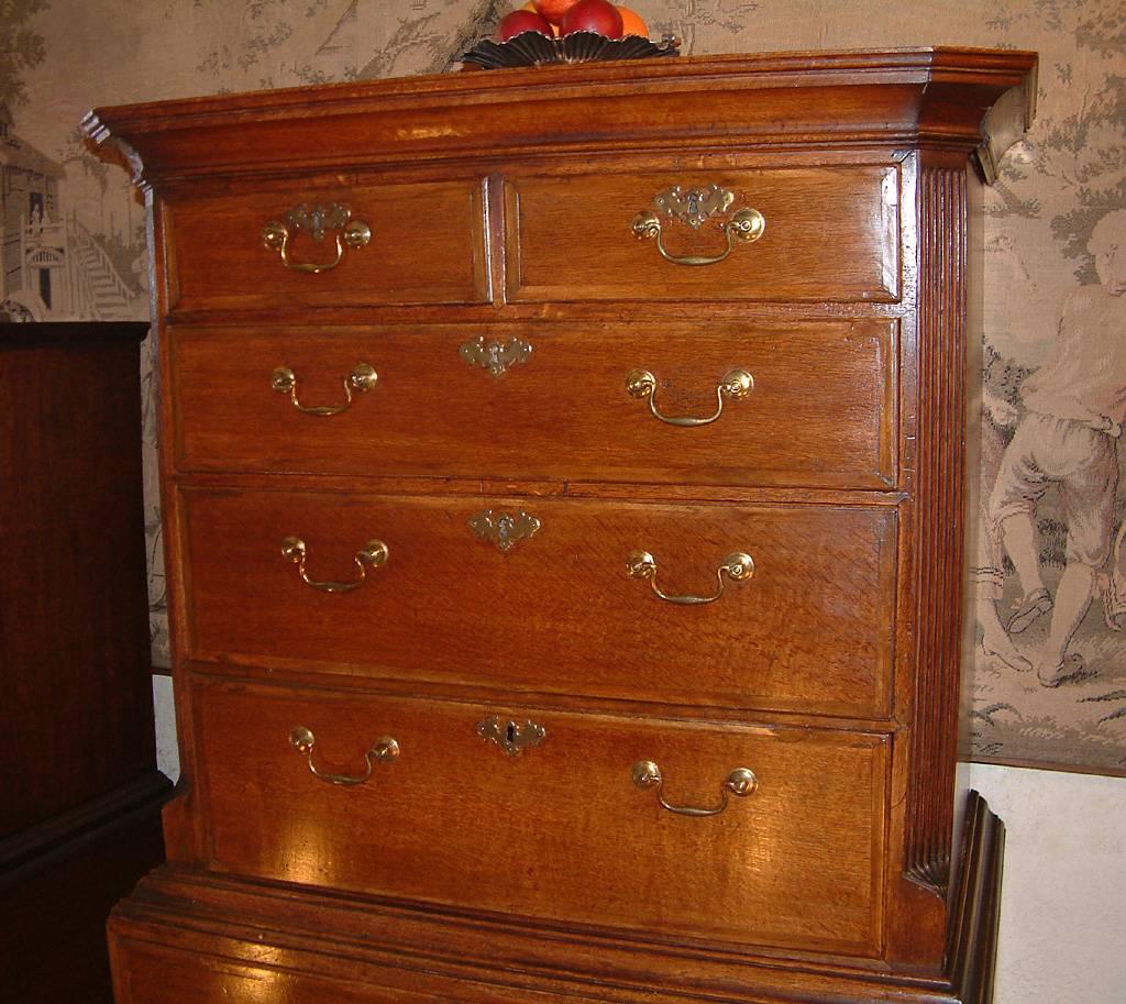 A small George II period oak chest on chest dating from circa 1750. The top with stepped concave cornice with canted corners above two short and three long Walnut banded Oak drawers with brass escutcheons and handles and with canted reeded corners.