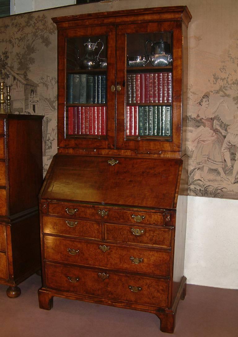 An early 18th century burr walnut bureau bookcase dating from circa 1720. The bookcase top with stepped concave cornice above a pair of glazed doors with original lock and working key. The bookcase interior with two adjustable shelves and three