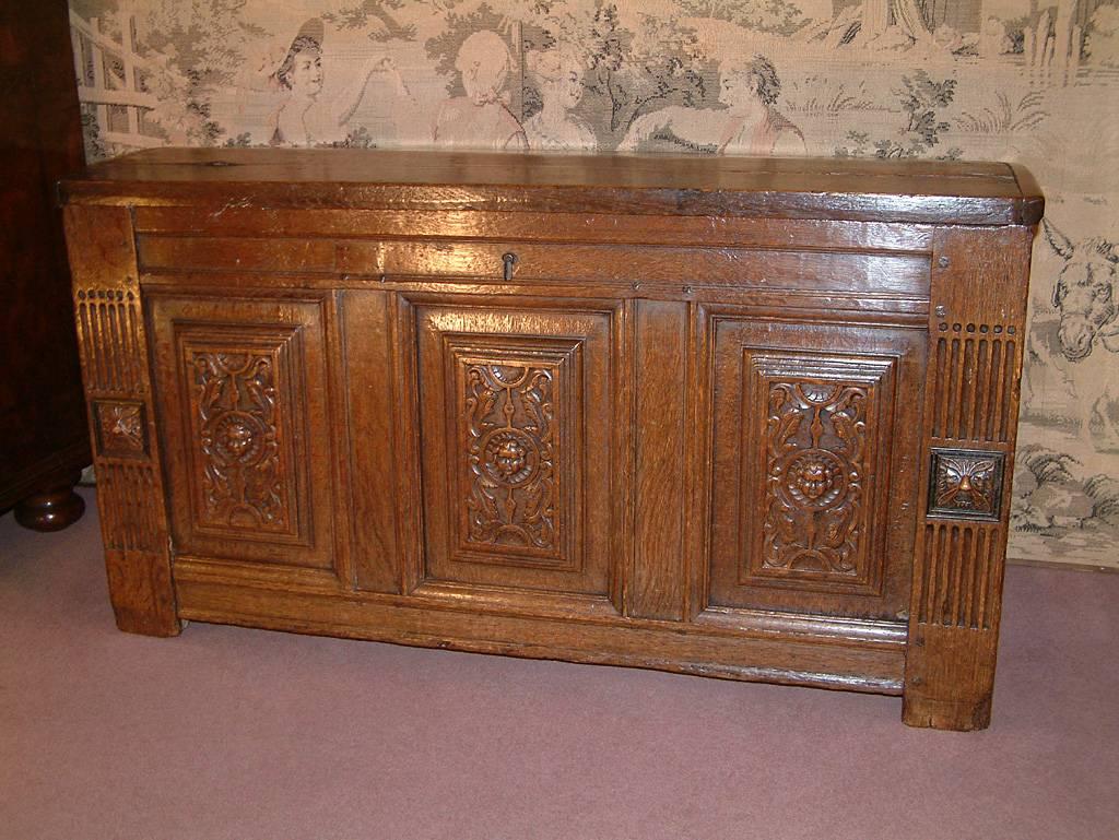 An early 17th century oak coffee with carved date 1614. The slightly domed planked top with cleated ends above a floral and cherub carved paneled front flanked by grooved and carved side supports terminating in stile feet. The coffer sides similarly