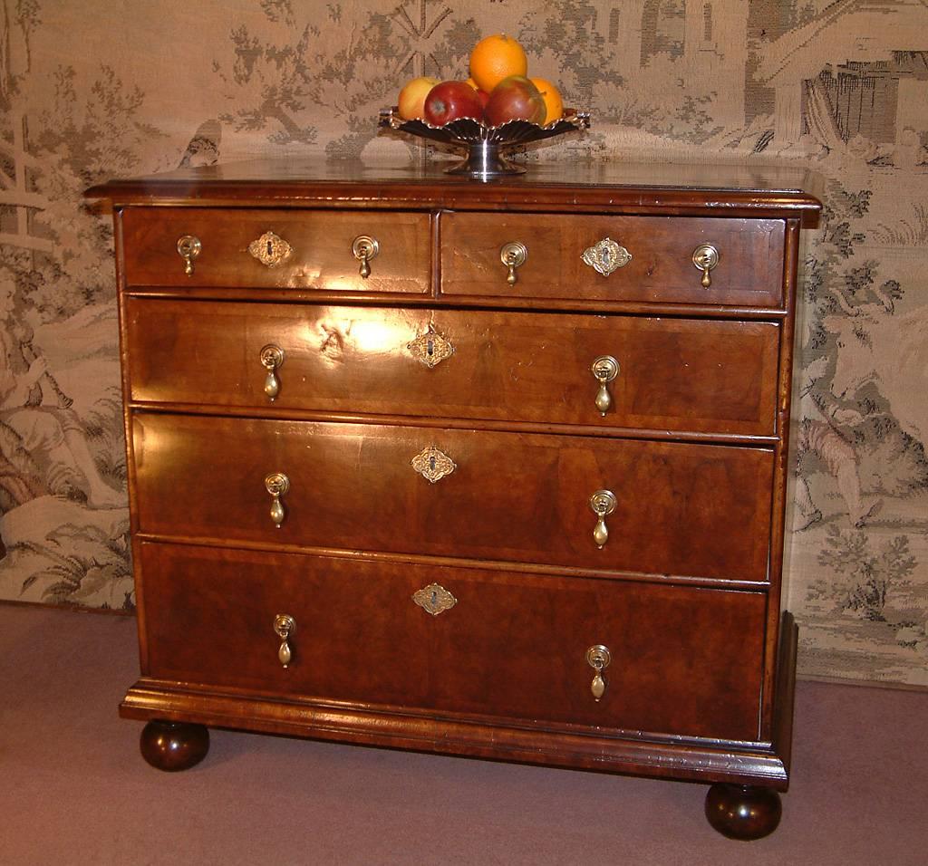 A Queen Anne period walnut bachelors chest dating from circa 1710. The rectangular top with crossbanding and moulded edge above two short and three long graduating crossbanded drawers with brass drop handles and escutcheons, with split moulded