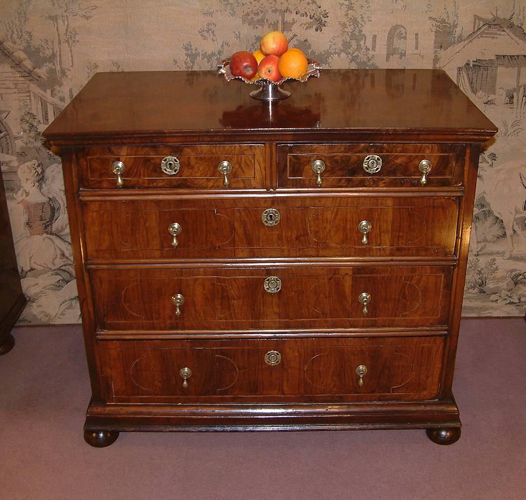 A late 17th century, William and Mary period figured Walnut chest of drawers c 1690. The quarter veneered cross banded top above two short and three long graduated side hung drawers with ebony and holly stringing and brass drop handles and