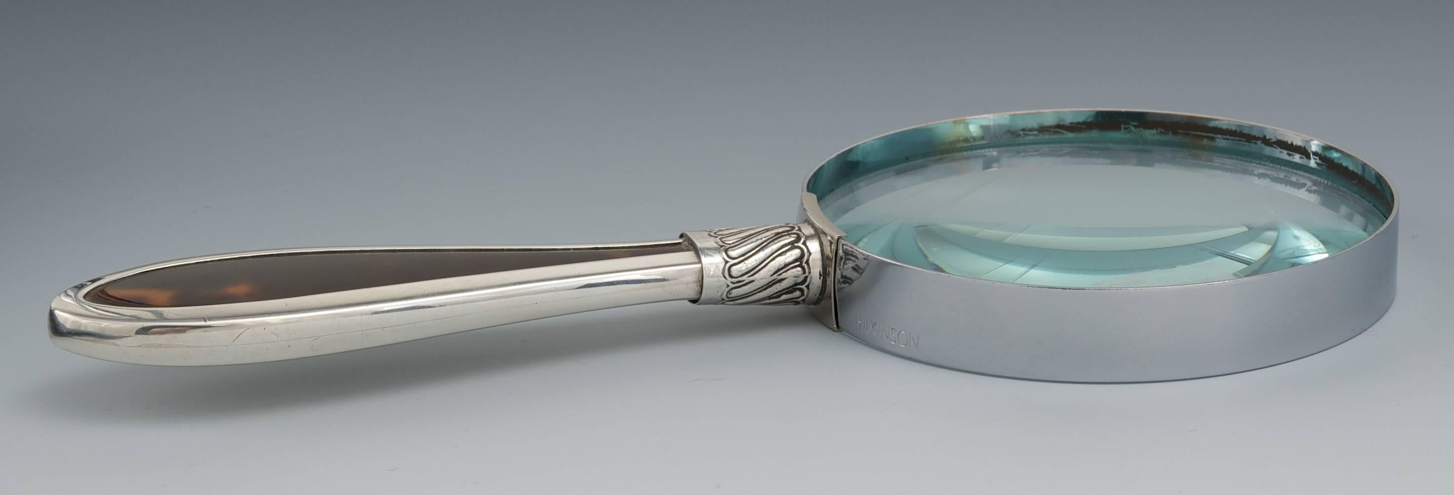 Hilkinson silver handled magnifying glass with tortoise shell inset

Measuring: 8" L, 3 ½" D lens, with a silver handle with a tortoise shell inset, repousse collar, marked with London marks, maker's mark (Hilkinson), date letter