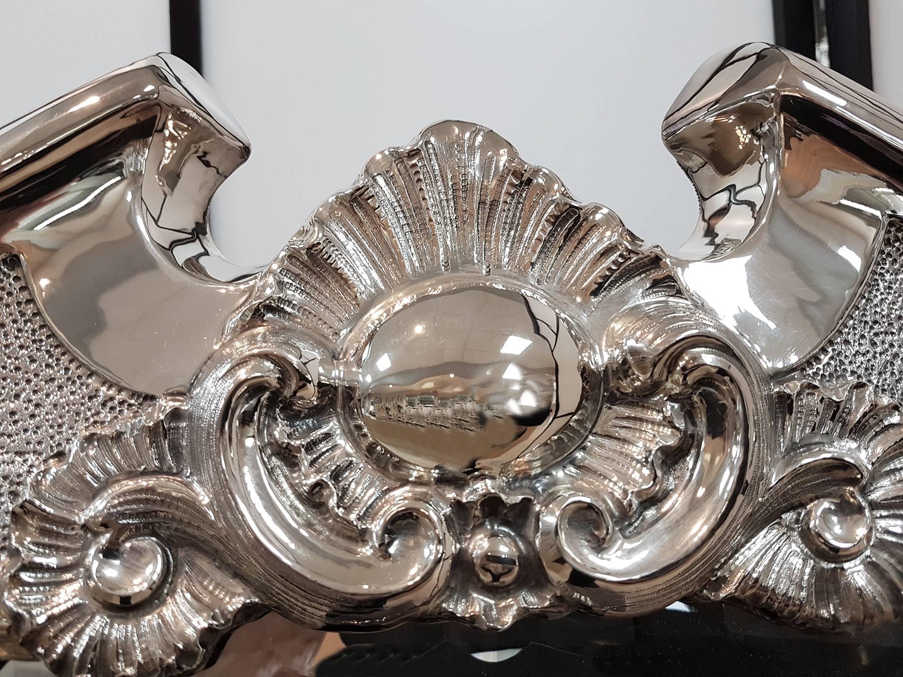 This Italian Baroque style mirror has a shaped silver frame that is embossed and chiseled. Certain central details were lightly hammered out in order to create a contrast with the shiny surfaces of the swirls that distinguishes the Baroque style.