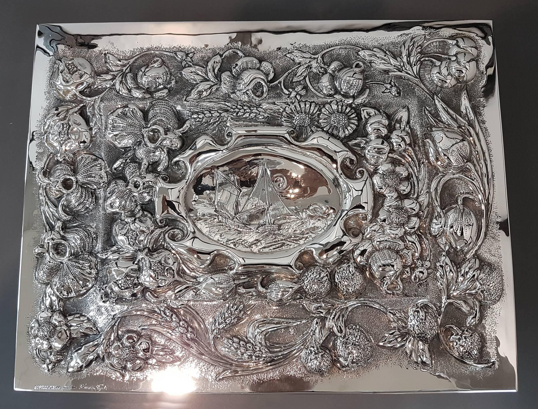 Rectangular solid silver 800°°/°°° table box.
The box is embossed by hand with flowers, leaves and fruits.
At the center of the hinged lid is embossed and engraved a sailing ship in a cartouche
The entire box was made entirely by hand.
The extensive
