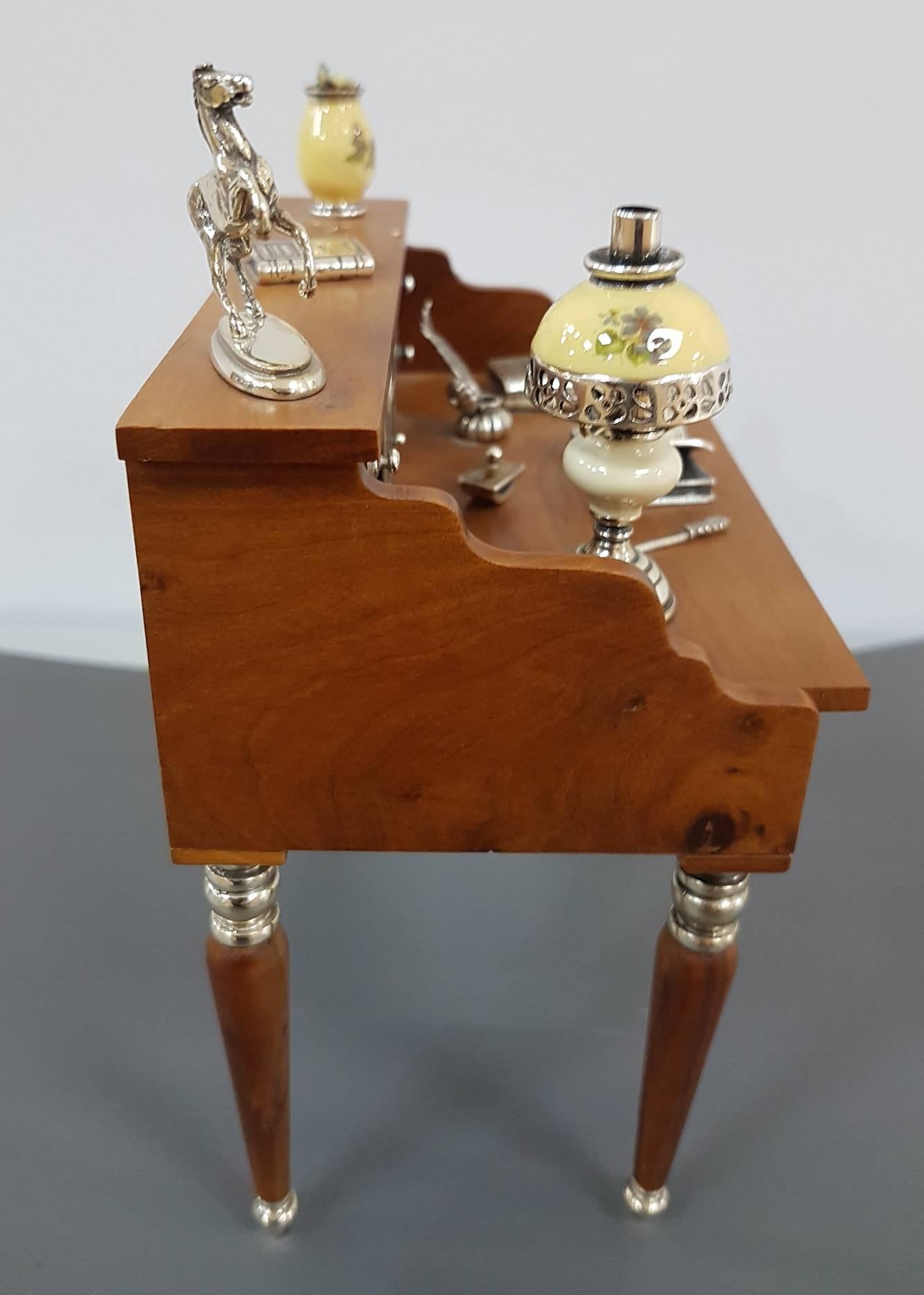 Miniature of antique writing desk made entirely by hand in briar with details in sterling silver.
The desk drawers are all open able and the details of the lamp and the vase is in enamelled sterling silver.