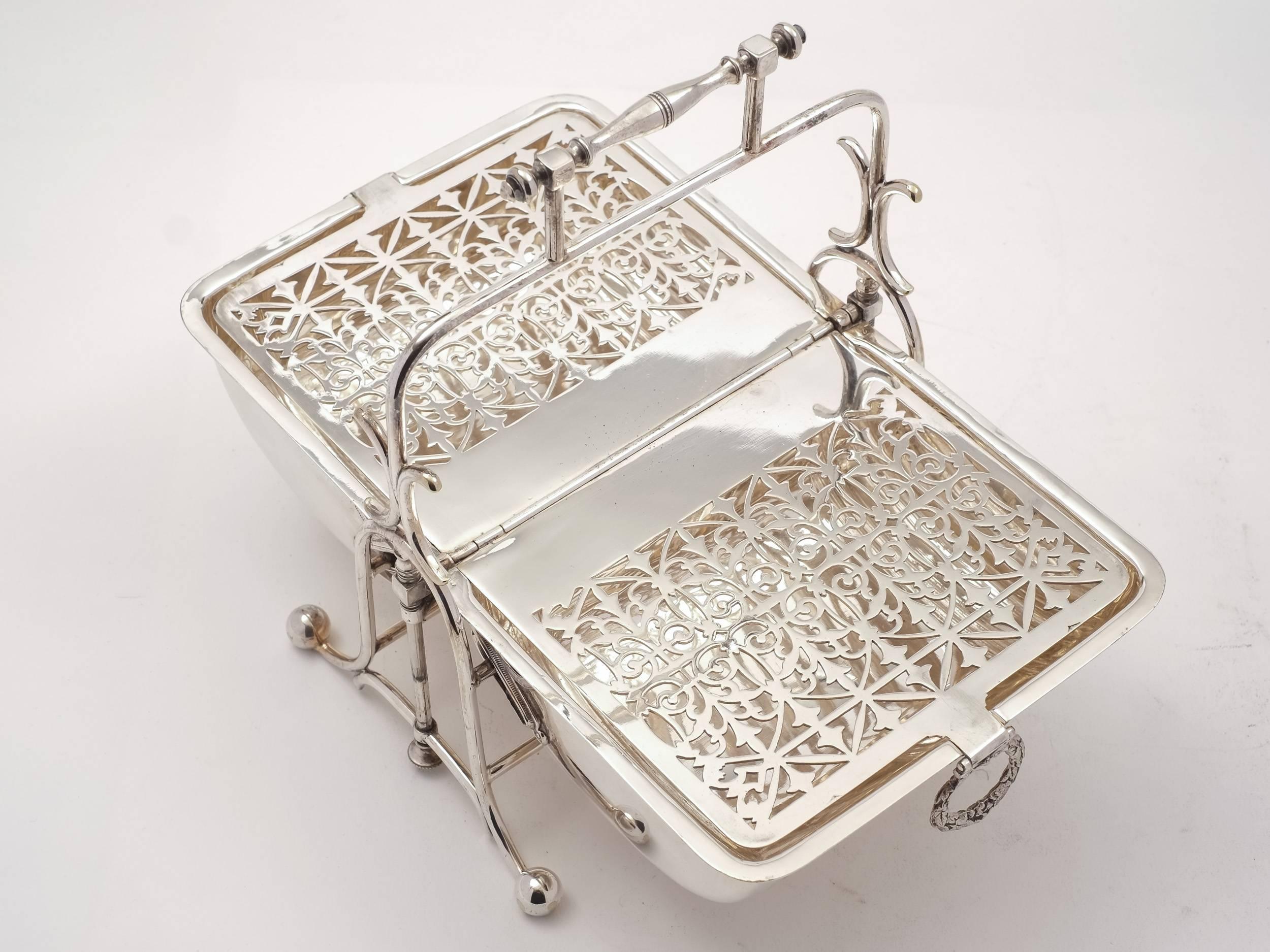 A fabulous English Victorian silver plated folding biscuit or cookie box which sits in frame and has carrying handle. When opened, two biscuit compartments with pierced lids are revealed. The lids (which secure the biscuits) fold up to centre to