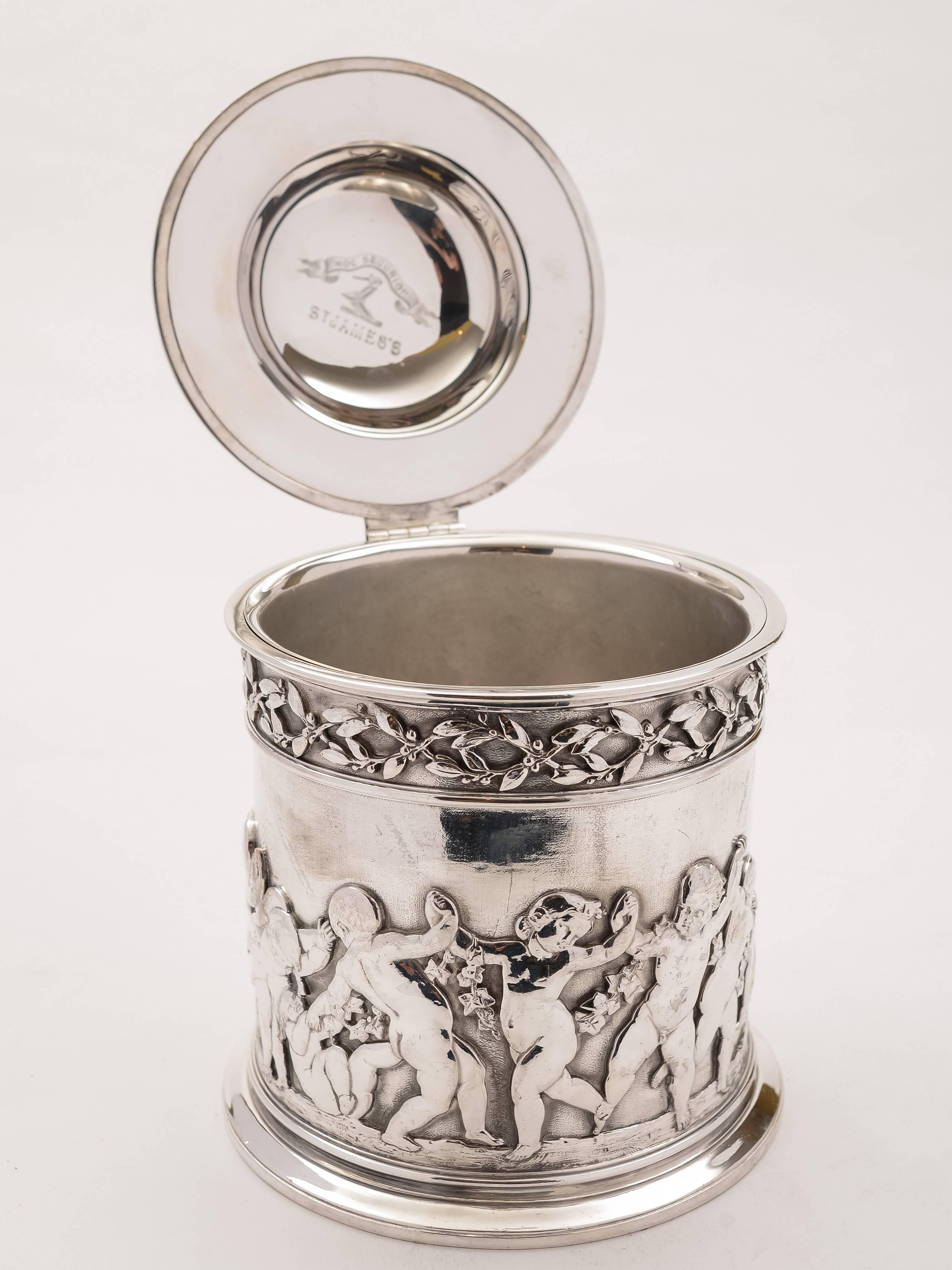 A stunning large English Victorian silver plated biscuit barrel or cookie jar with embossed cherub decoration to body. Has engraved inside of the hinged lid which has the family crest and motto 'Hoc Securior' and 'St James's', possibly connected to