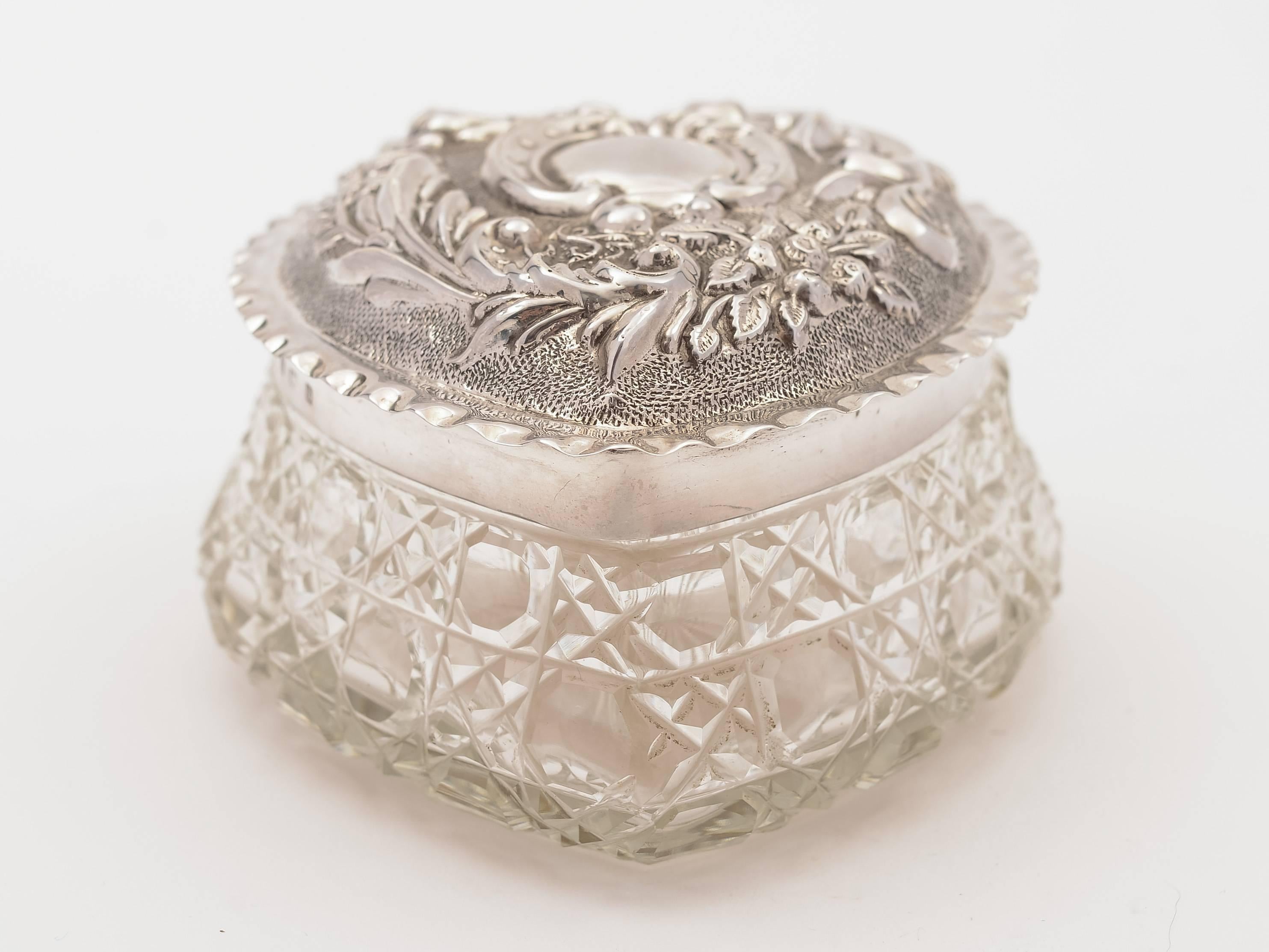 A sweet heart-shaped English sterling silver and hobnail cut-glass trinket box. The lid is beautifully embossed with flower motif and has vacant cartouche to centre with gilded interior to lid and star cut base. Hallmarked Birmingham 1901.