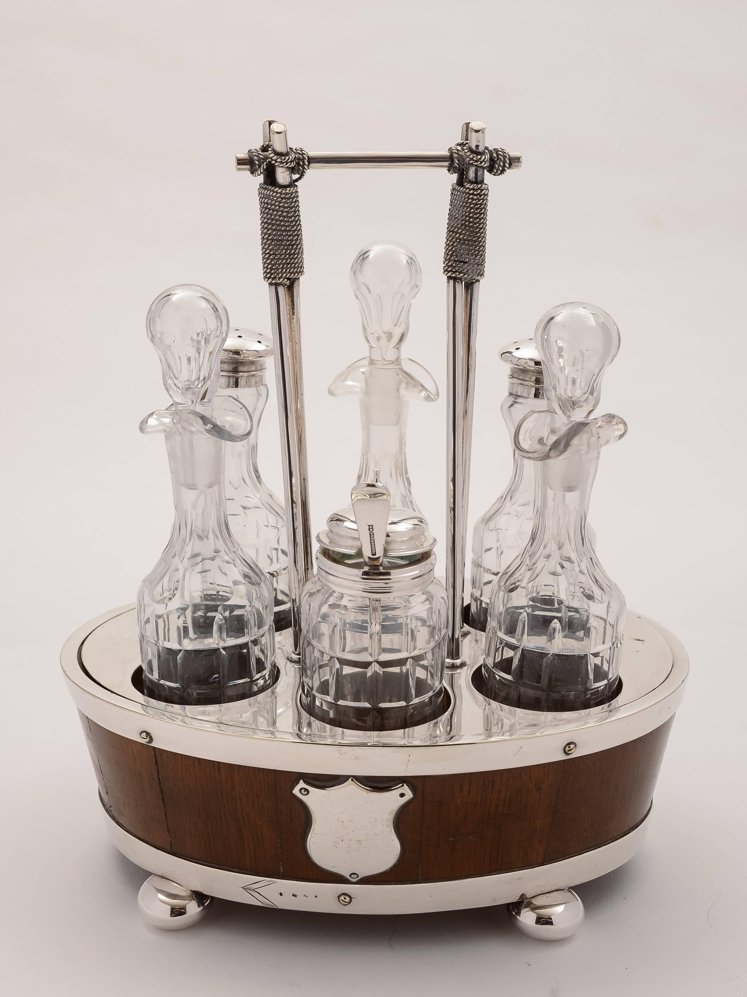 A fabulous English oak and silver plated cruet which consists of six cut-glass bottles, three for oil and vinegar, two bottles with sifter tops and one mustard pot. They stand in an oak and silver plated frame which has vacant cartouche shields to