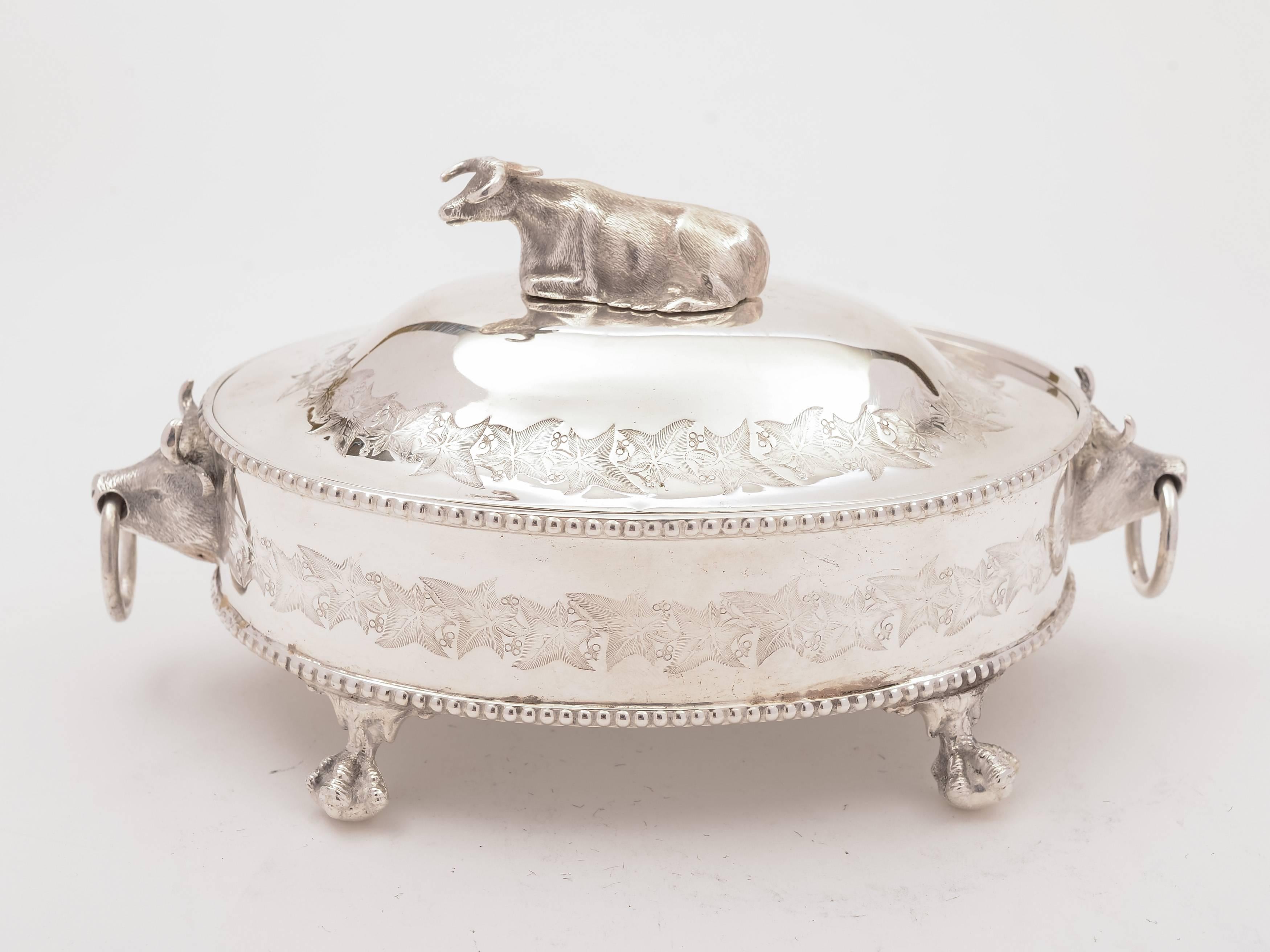 A lovely English Victorian silver plated butter dish. Decorated with bulls heads to each end, a cow finial and engraved ivy leaf decoration to top and sides. Stands on four ball and claw feet and has a frosted glass liner, circa