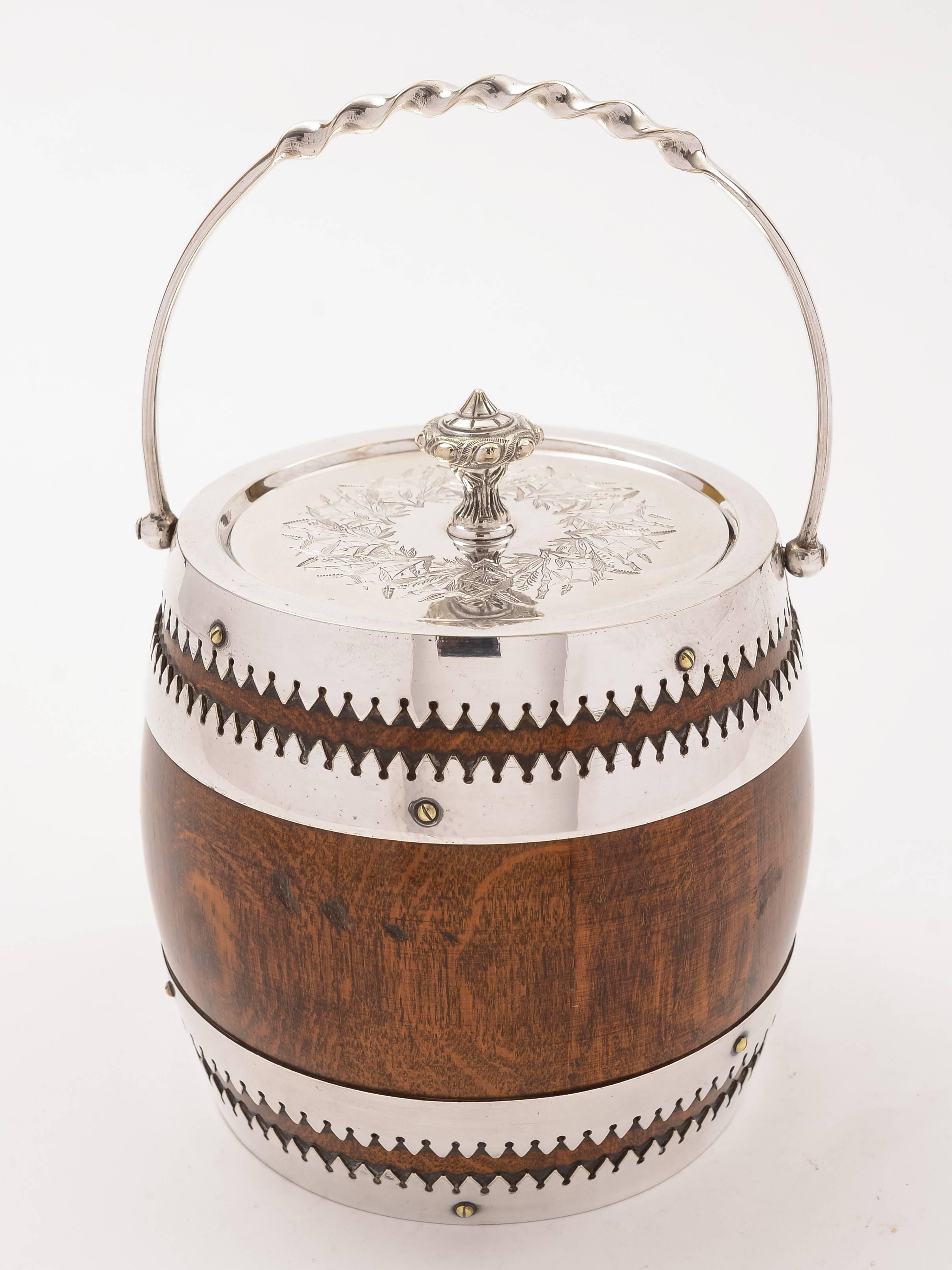 A fabulous English Victorian oak and silver plated biscuit barrel with white china liner and folding handle. The lid has engraved decoration and there is a vacant shield cartouche to front of barrel, circa 1890.

Free worldwide delivery.
