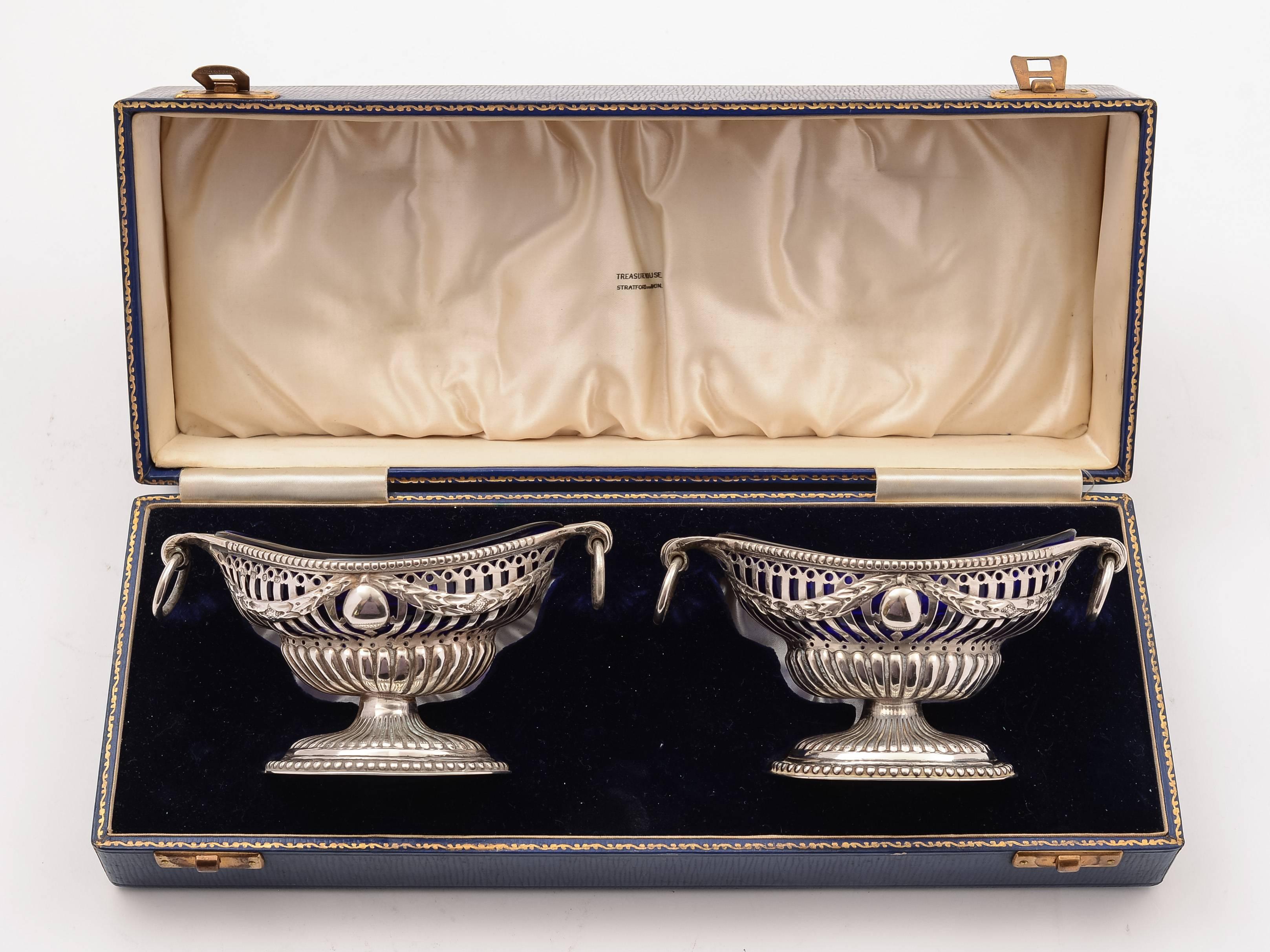 A fabulous cased pair of English Victorian silver salts in the Georgian style with pierced and embossed decoration, ring handles and cobalt blue glass liners. Marked 'H & H' for the maker Harrison & Hipwood and hallmarked Birmingham,