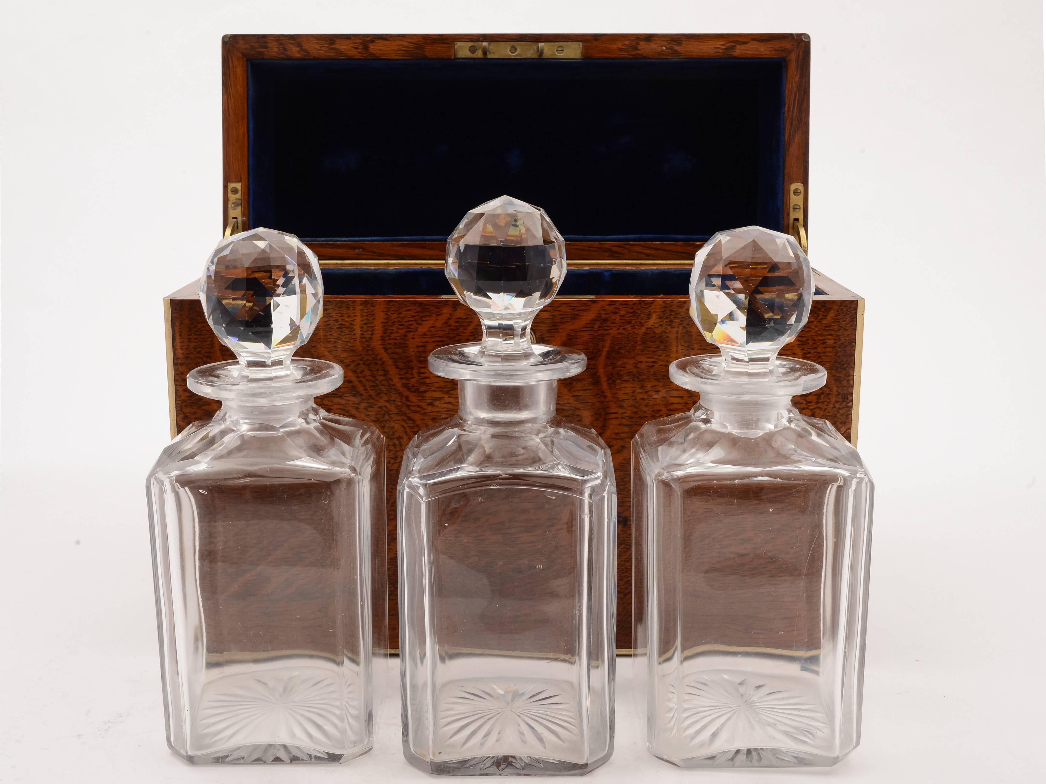 A beautiful Victorian three bottle tantalus in oak case which is edged with brass and has three blue velvet-lined compartments. The lid is blue velvet lined and has a brass lock with original key. Inside the box are three matched square cut glass