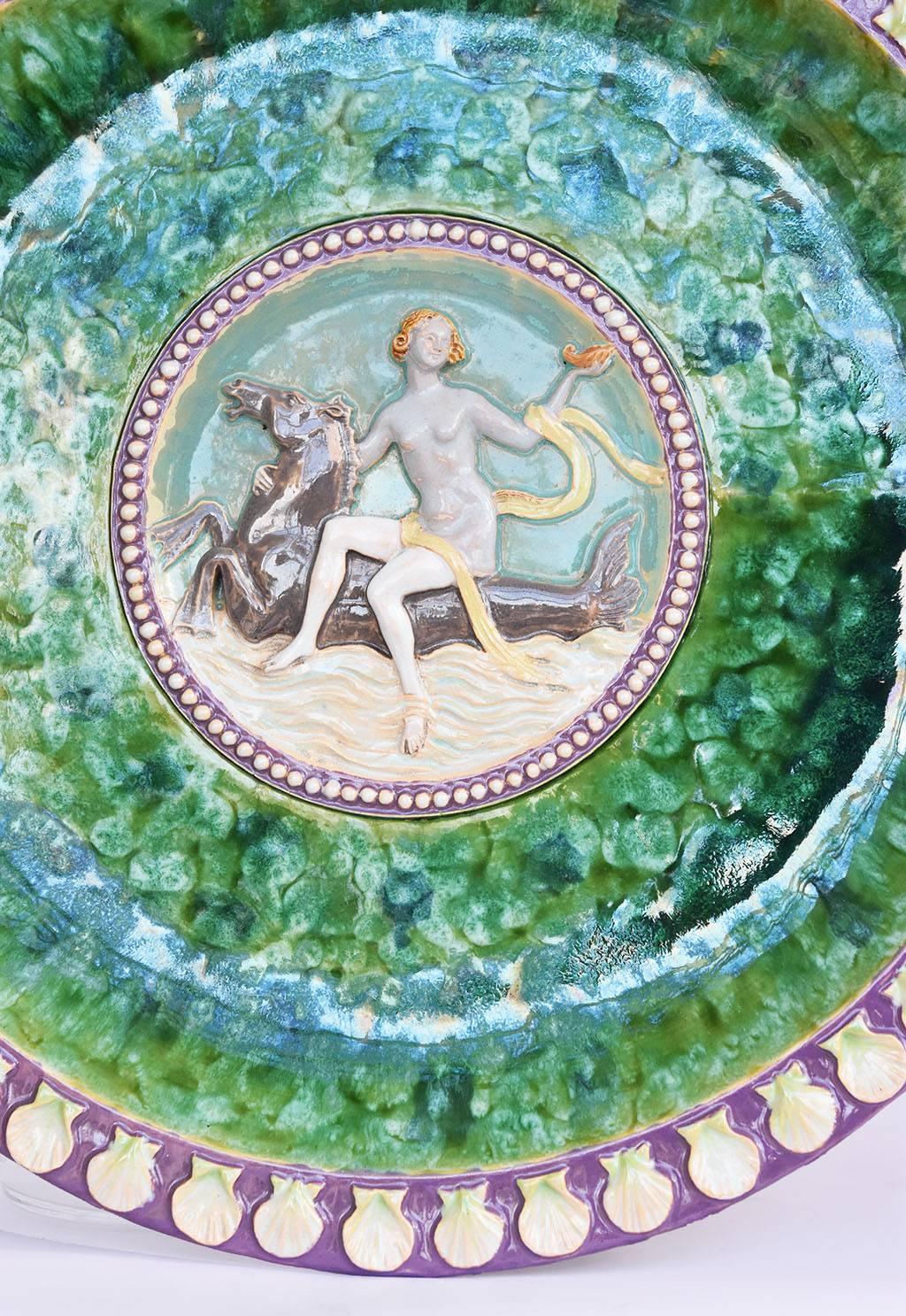 A very rare and striking Austrian terracotta majolica glazed charger, circa 1895
The body decorated in mottled sea green and blue, a central medallion depicting Aphrodite riding a hippocamp within a band of white pearls against a deep lavender