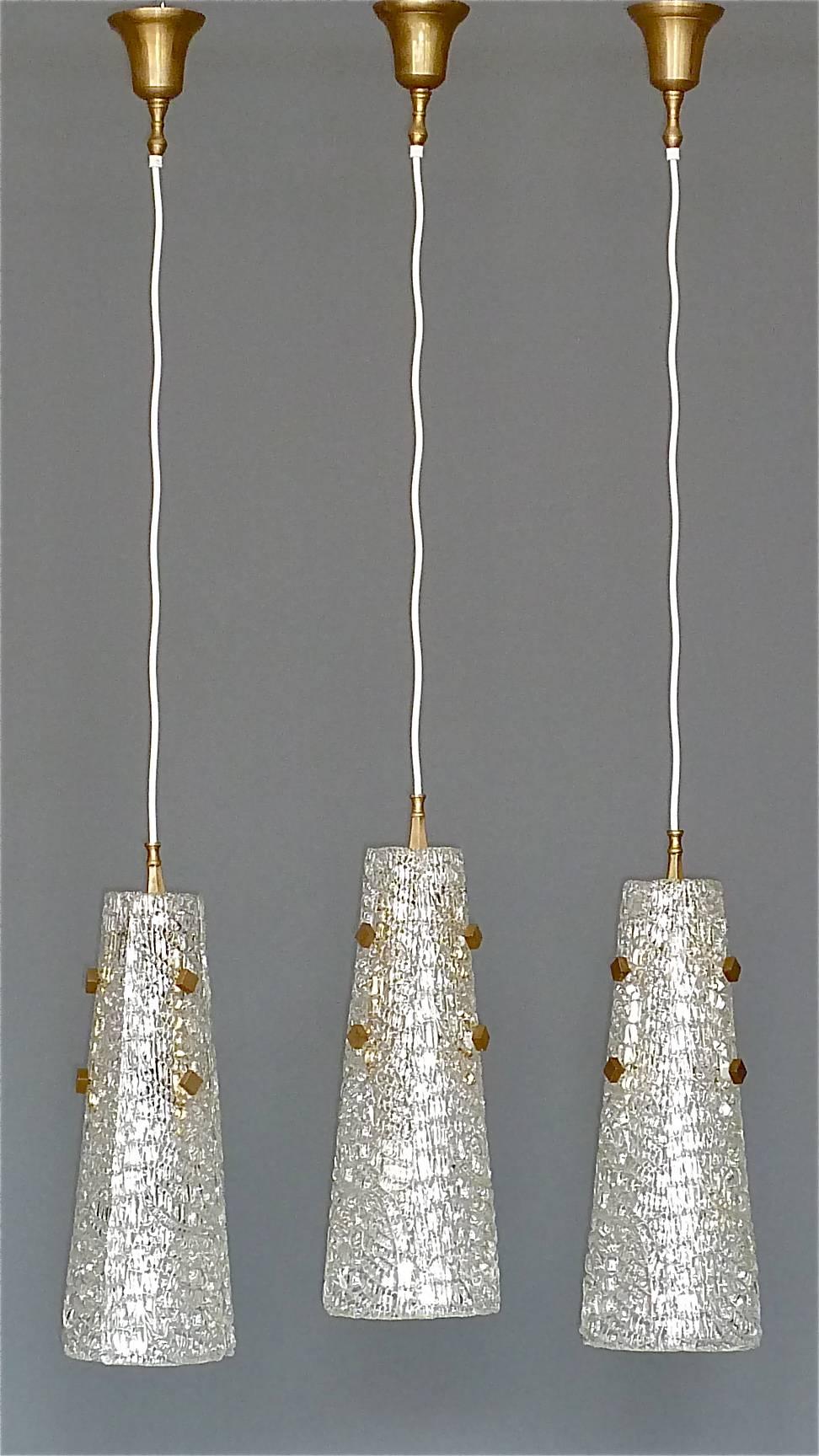 Rare and early set of three J.T. Kalmar midcentury pendant lamps of textured Murano ice glass, Austria, circa 1950s. The large lights are made of three glass petals forming a cone shade and beautiful patinated brass details. One pendant takes three