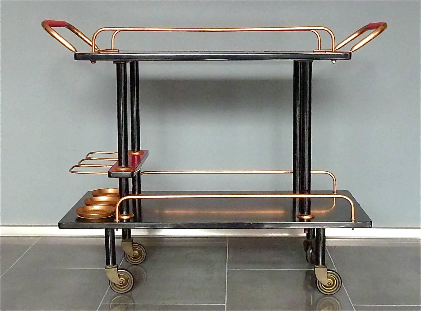 A rare and unique Bauhaus vintage bar cart or serving trolley with black painted wood, black painted iron, patinated copper details, some kind of red formica foil surface and red plastic around handles. Made in Germany, circa 1930s to 1950s in a