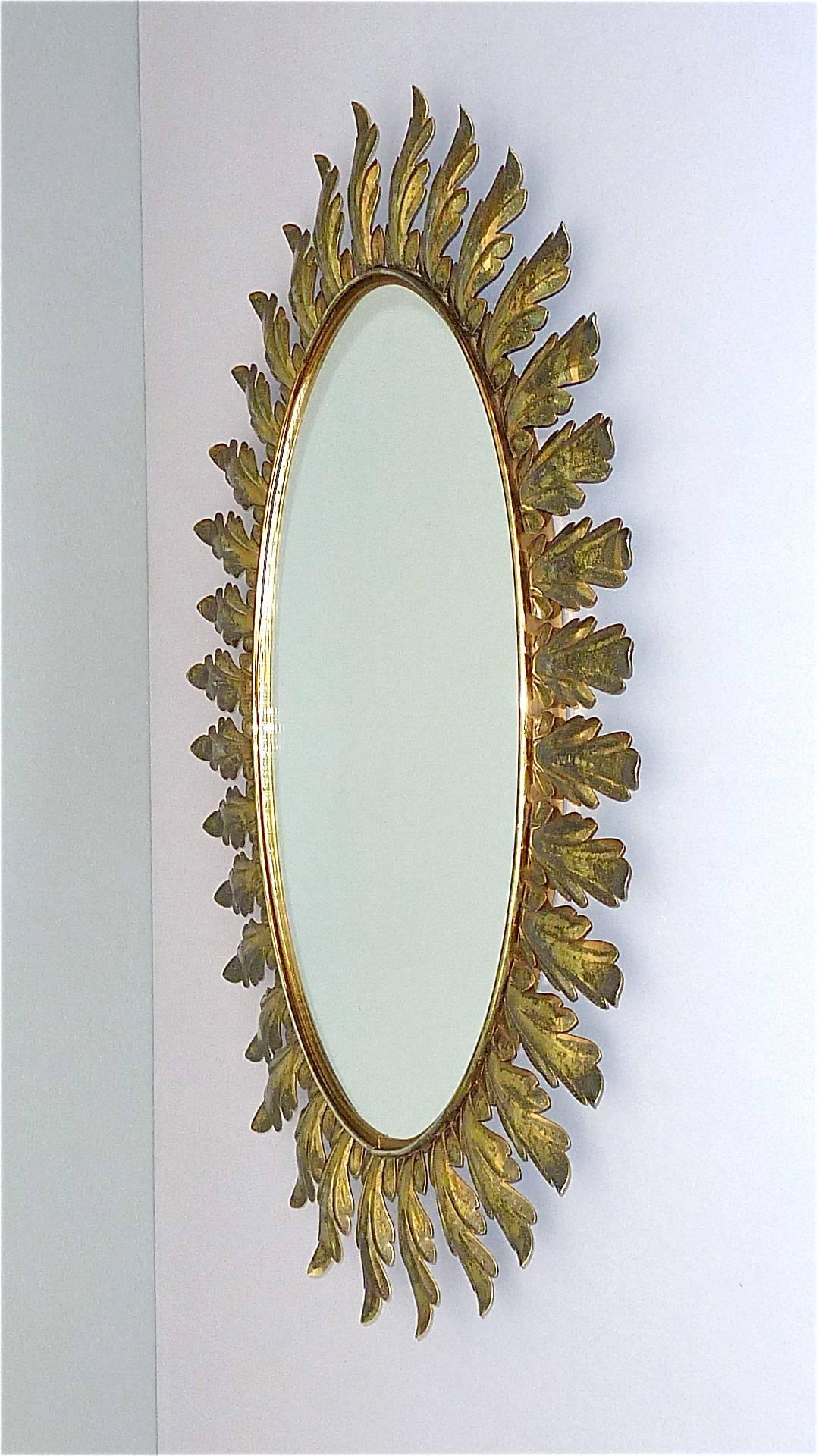 Large and fabulous of vintage Midcentury starburst sunburst wall mirror made in Belgium around 1950. The big oval mirror is made of patinated brass and brass sheet metal mounted on a wood base with a still remaining paper label which reads Made in