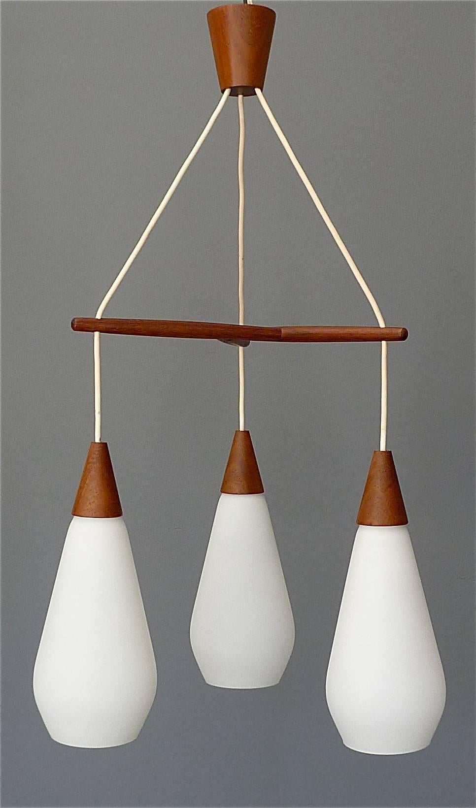 Fantastic sculptural Midcentury Scandinavian modern pendant teak lamp made around 1960 with attribution to Uno & Östen Kristiansson for Luxus / Sweden. The gorgeous light has three opaque white glass shades with satin finish hanging on a teak wood