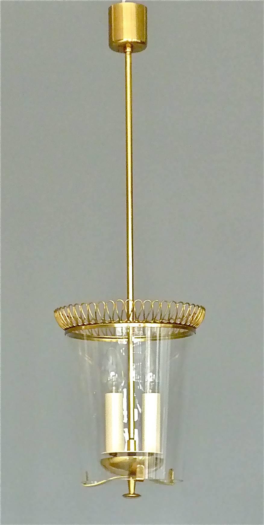 Rare brass and glass two-light midcentury pendant or lantern in the style of Josef Frank, Austria, 1950s. Beautiful patinated brass loop crown decoration to the upper rim of the old and original glass cylinder. The lower rim to glass with two tiny