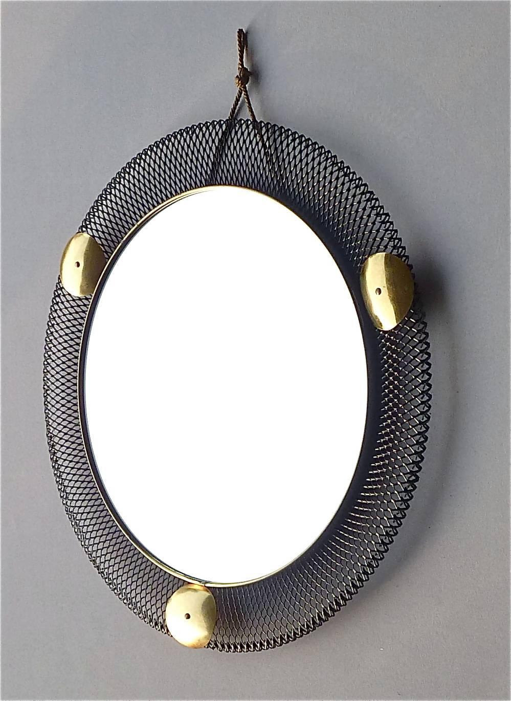 Round midcentury wall mirror which is made in the style of Jacques Biny, Mategot or Pierre Guariche, France or Italy, circa 1955. It is made of black lacquered or enameled stretched metal, lovely patinated brass details, mirror glass and its