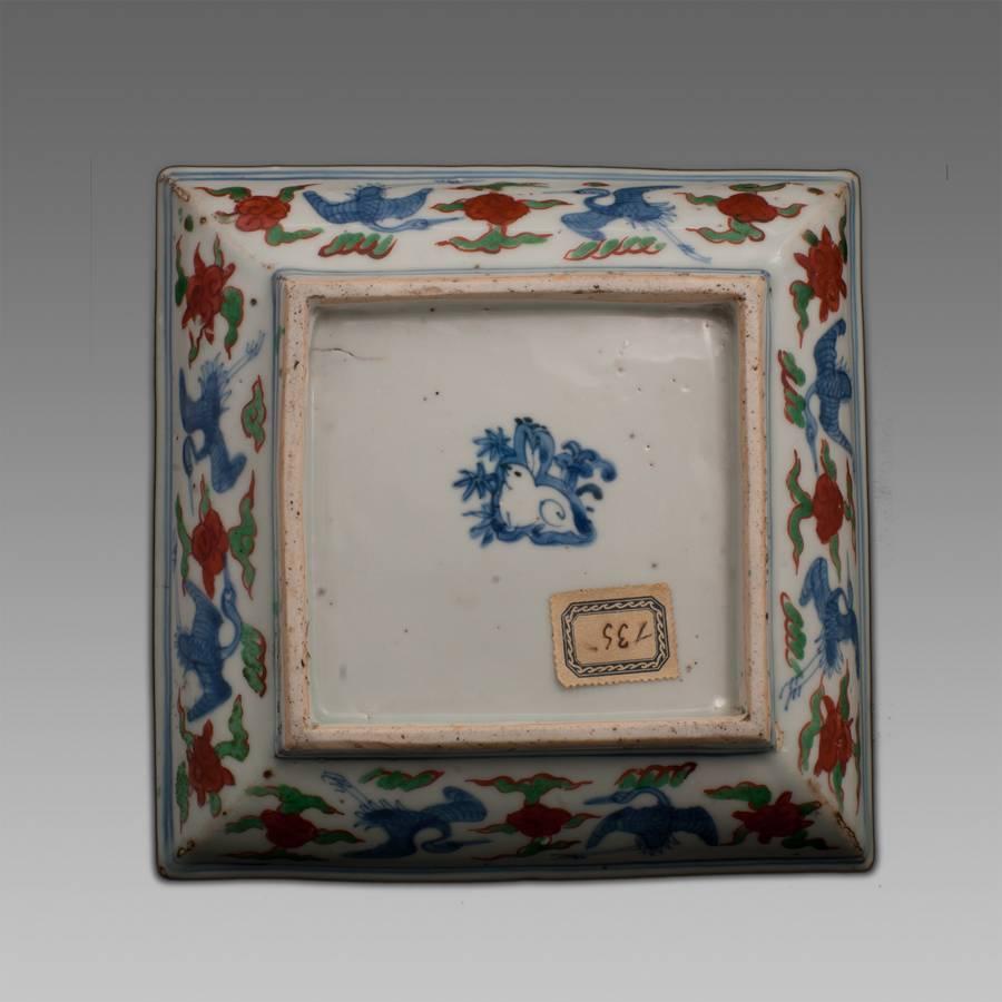 A Wucai porcelain square dish, decorated in cobalt underglazed blue and polychrome enamels with the rare feiyu winged dragon pattern in the centre. The borders with carps and aquatics plants. The back with cranes among clouds. The base with the