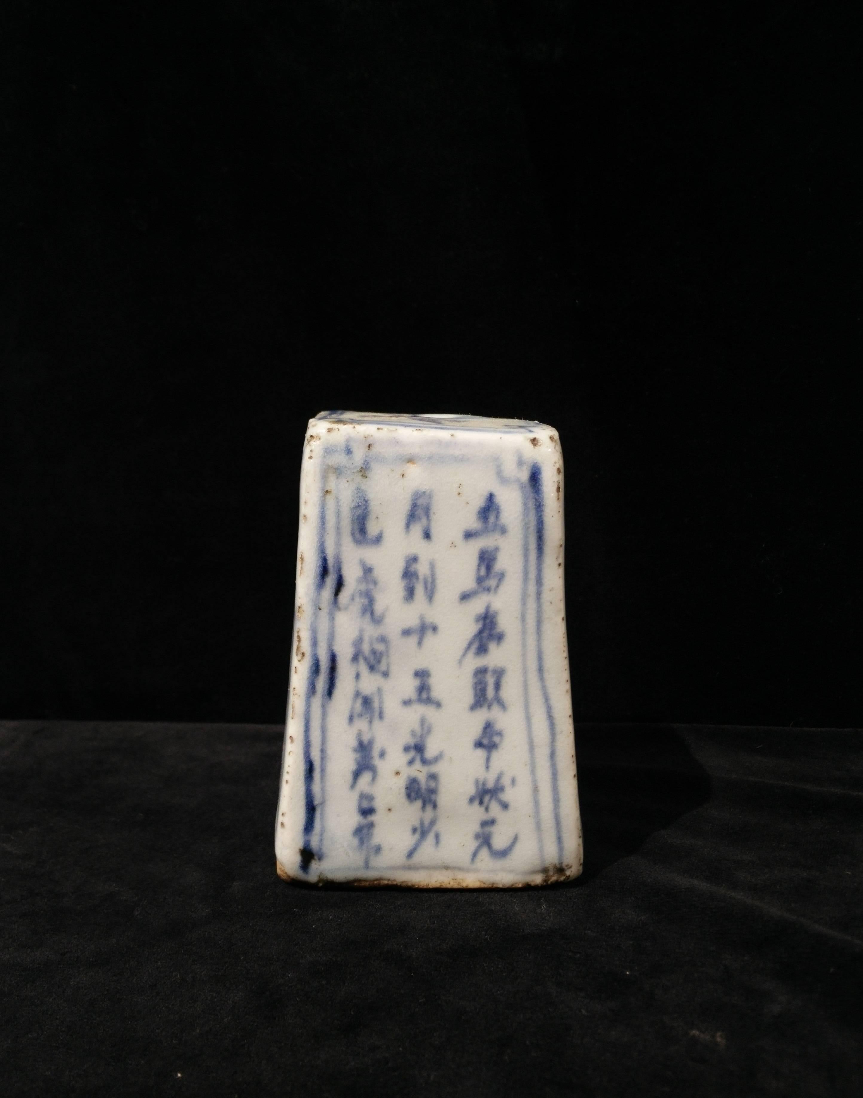 The water dropper, rectangular, painted in underglaze blue on the four sides. Two sides with inscriptions, one side depicting an official, one side with a lake landscape. The top with a central hole, the base unglazed with a hole.