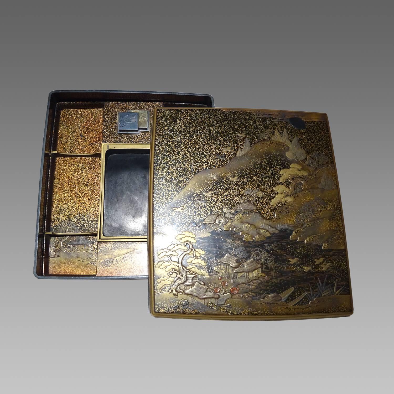The writing set in gold and silver lacquer with hardstones and lead inlays, using maki-e, hiramaki-e, takamaki-e and nashiji techniques. The suzuribako is decorated with houses in a landscape of mountains and river. The inside of the box showing a