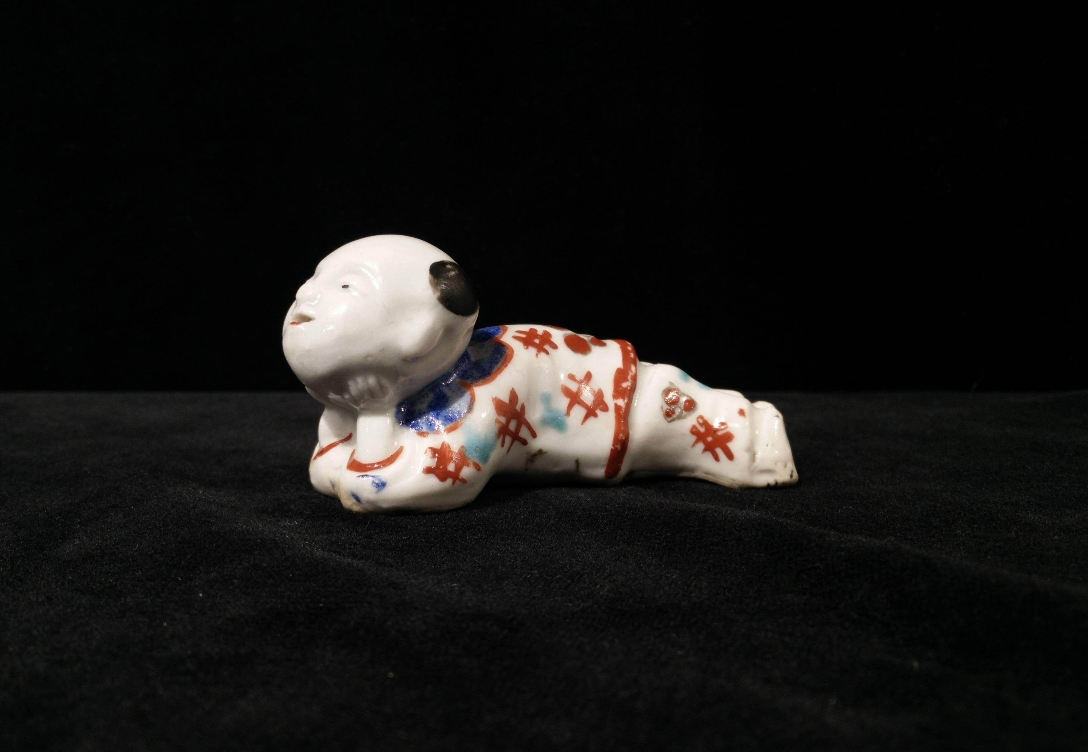 The whistle in form of a reclining boy with his head raised and supported by his hands. The whistle is blown through a slot in the feet and operated through a hole in the base and the open mouth. The details of the flowered robe are painted in red,