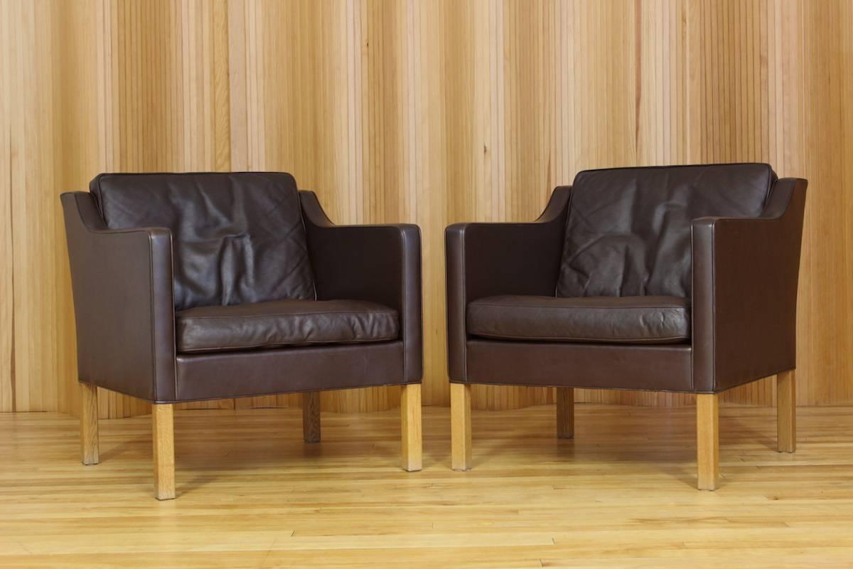 Pair of Borge Mogensen dark brown leather lounge chairs - model 2421 - manufactured by Fredericia Stolefabrik, Denmark. These examples have solid oak legs. Original paper label to the underside (see photo).

I have the matching three-seat sofa