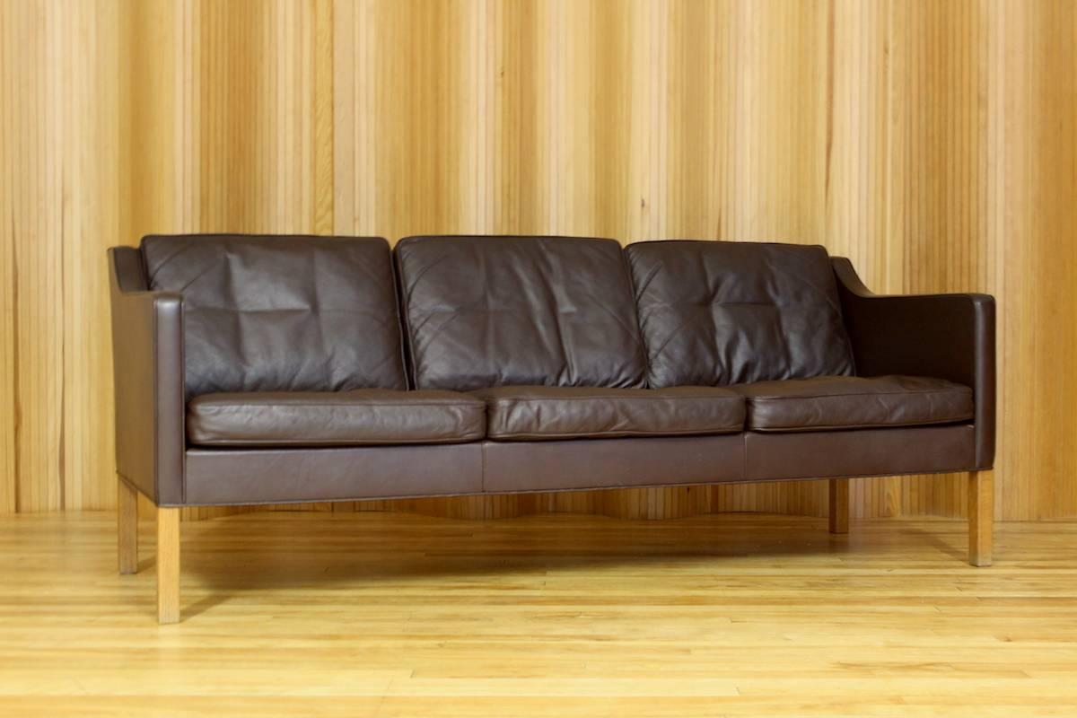 Børge Mogensen three-seat dark brown leather sofa - model 2423 - manufactured by Fredericia Stolefabrik, Denmark. This example has solid oak legs. Original paper label to the underside (see photo).

I have the matching pair of lounge chairs also