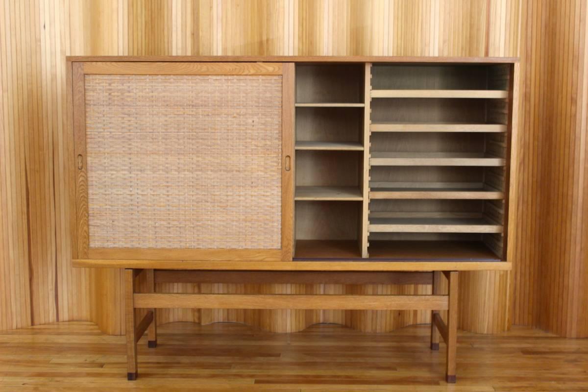 Description: Stunning and very rare oak highboard with sliding rattan doors. 

Designer: Hans J Wegner

Manufacturer: Ry Mobler, Denmark

Date: Date stamped for 27th April 1962

Dimensions: Length 180cm; Depth 49cm; Height