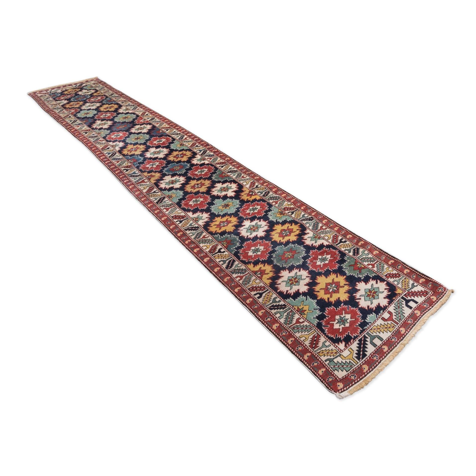Hall rug of the Caucasus region.
- Made in the first quarter of the 20th century
- Typical design of this region, a succession of small format palmettes follow one another throughout the central field.
- Colors, in greens, yellows, reds and blues