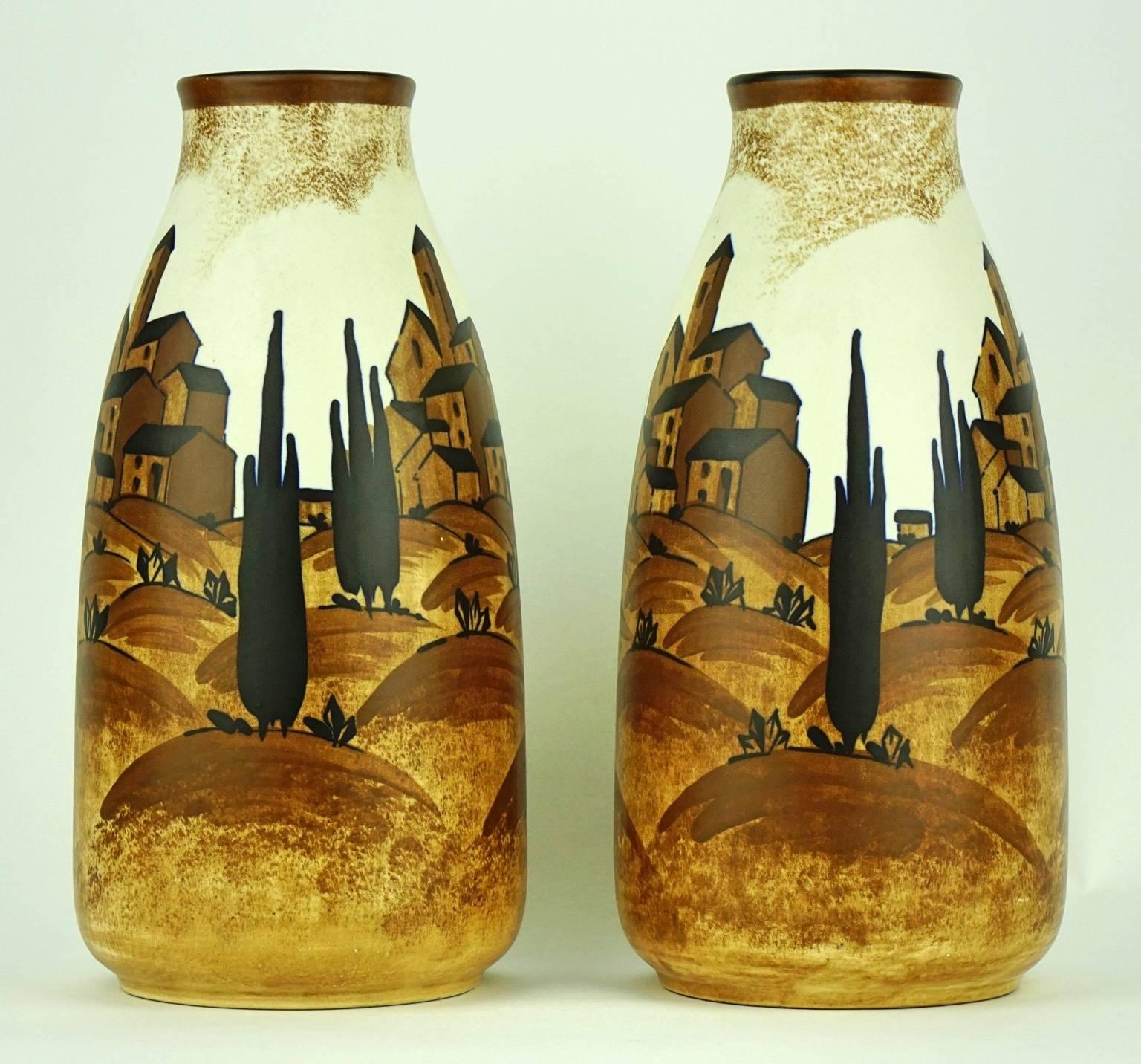 This pair of rare Art Deco matte vases with a Mediterranean landscape in ochre hues is an example of an Art Deco style which avoids the showiness of colours and ensures the connection between material and design.

It is signed C. Catteau with ink,