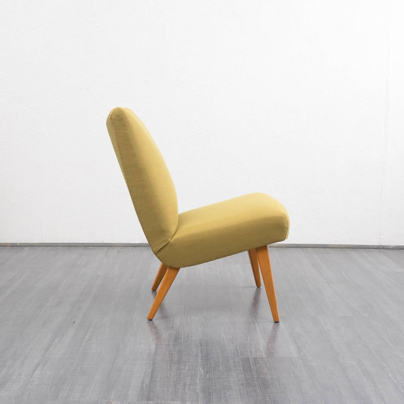 Shapely armchair from the 1950s.

Straight-lined design with slanted solid beech legs, typical of the time. The original barrel-arbor cushion has been reupholstered with new foam and newly covered with a high-quality green-yellow upholstery