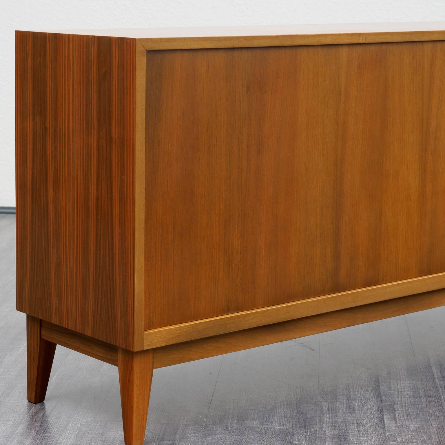 Slim sideboard from the 1950s. Design by Georg Satink for WK Möbel, 1952. Walnut veneer. High-quality workmanship, sliding doors with nice handles.

The top has been stored by the cabinet maker. Very good condition with small traces of usage.