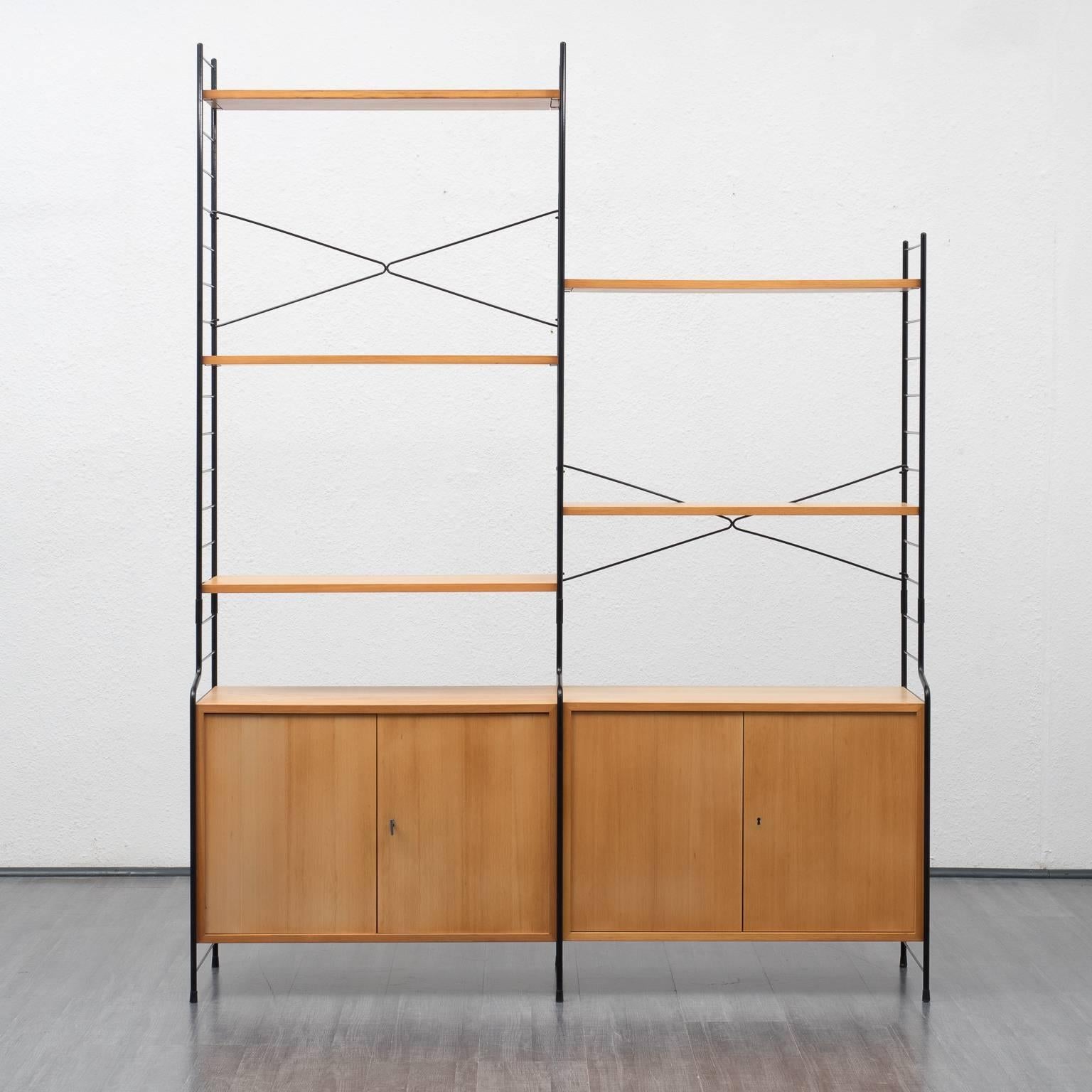 Free-standing shelving system by WHB from the 1960s. Black metal ladders and black metal handles. Five elm veneered shelves and two containers with lockable double doors and shelves inside.

Good condition with small traces of usage.