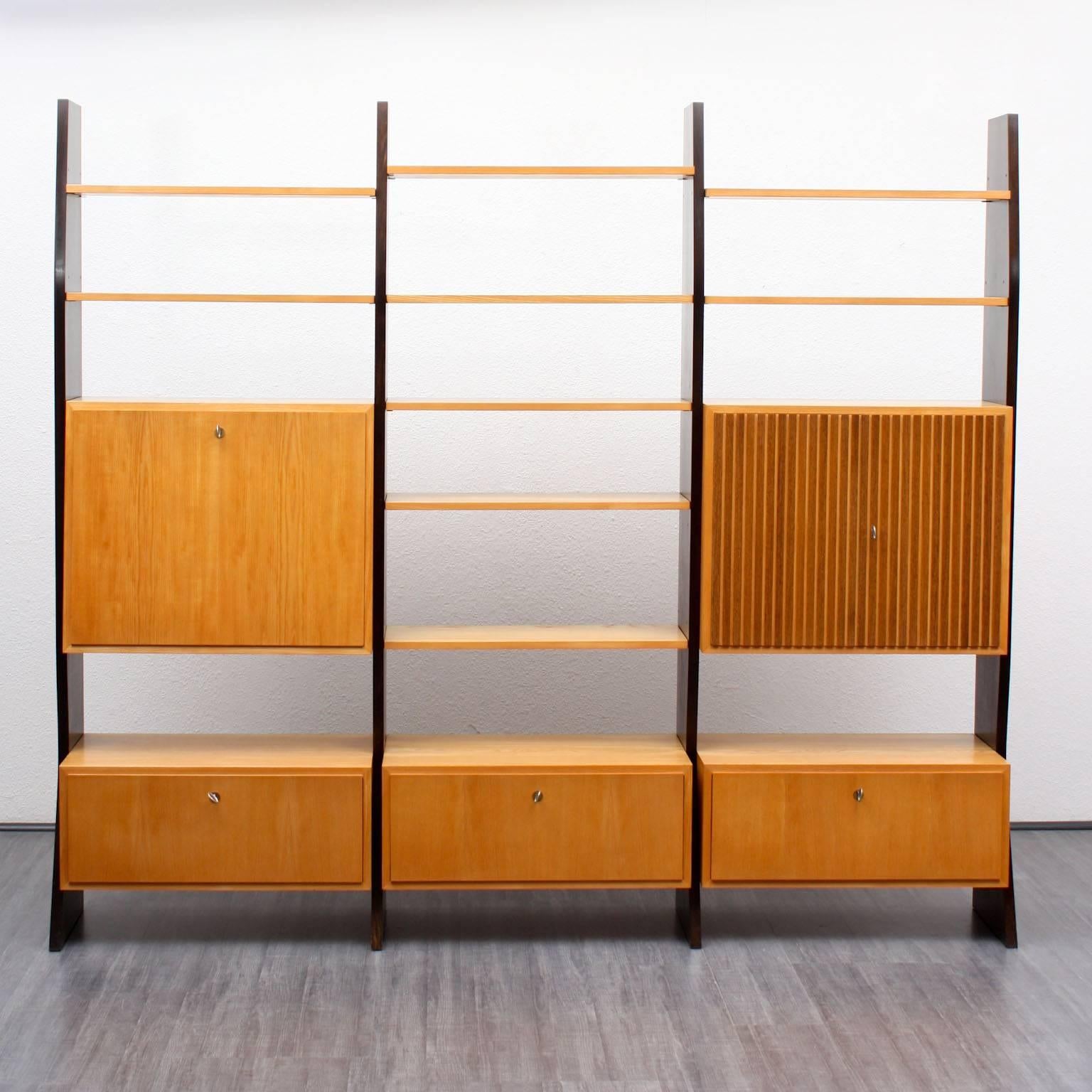 Large shelf from the 1950s. Witty, bicoloured design by Erich Stratmann for Idee Möbel. Elm-faced with dark brown varnished side panels. Nine shelves, one container with illuminated secretary and four lockable containers in two sizes.

Good