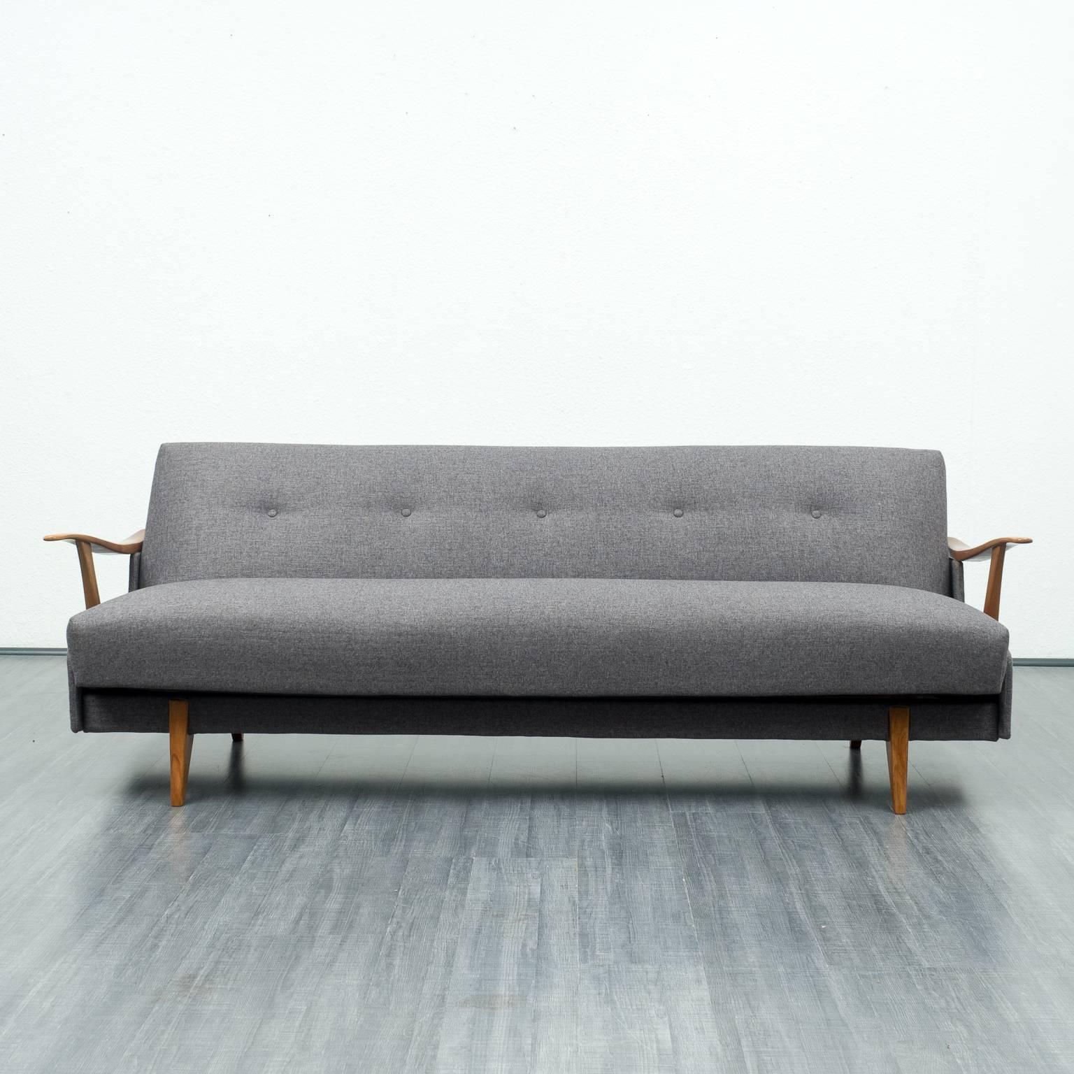 Shapely streamline sofa from the 1950s. Solid walnut armrests and feet. In no time at all the sofa changes into a comfortable guest bed with a lying surface of 194x100cm. The original innerspring cushions were professionally reupholstered and