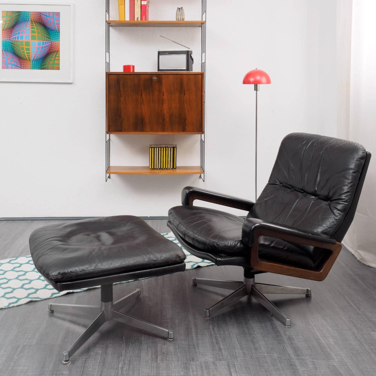 A Swiss made design classic from the 1970s:
The King chair by Strässle in black leather with rosewood armrests. High-quality materials and workmanship. The chair comes with the matching foot-stool. Good original condition with small traces of wear