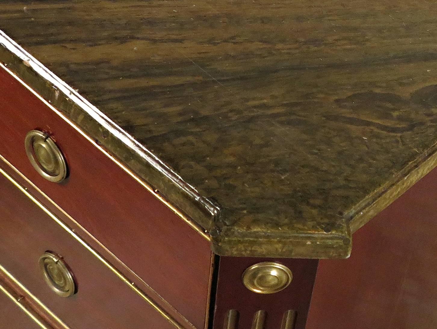 A Russian Neoclassical Brass Mounted Mahogany Commode 
Early 19th Century 

The rectangular faux marble top with outset square corners, above a conforming case fitted with three long graduated drawers, flanked by fluted stiles headed by roundels and