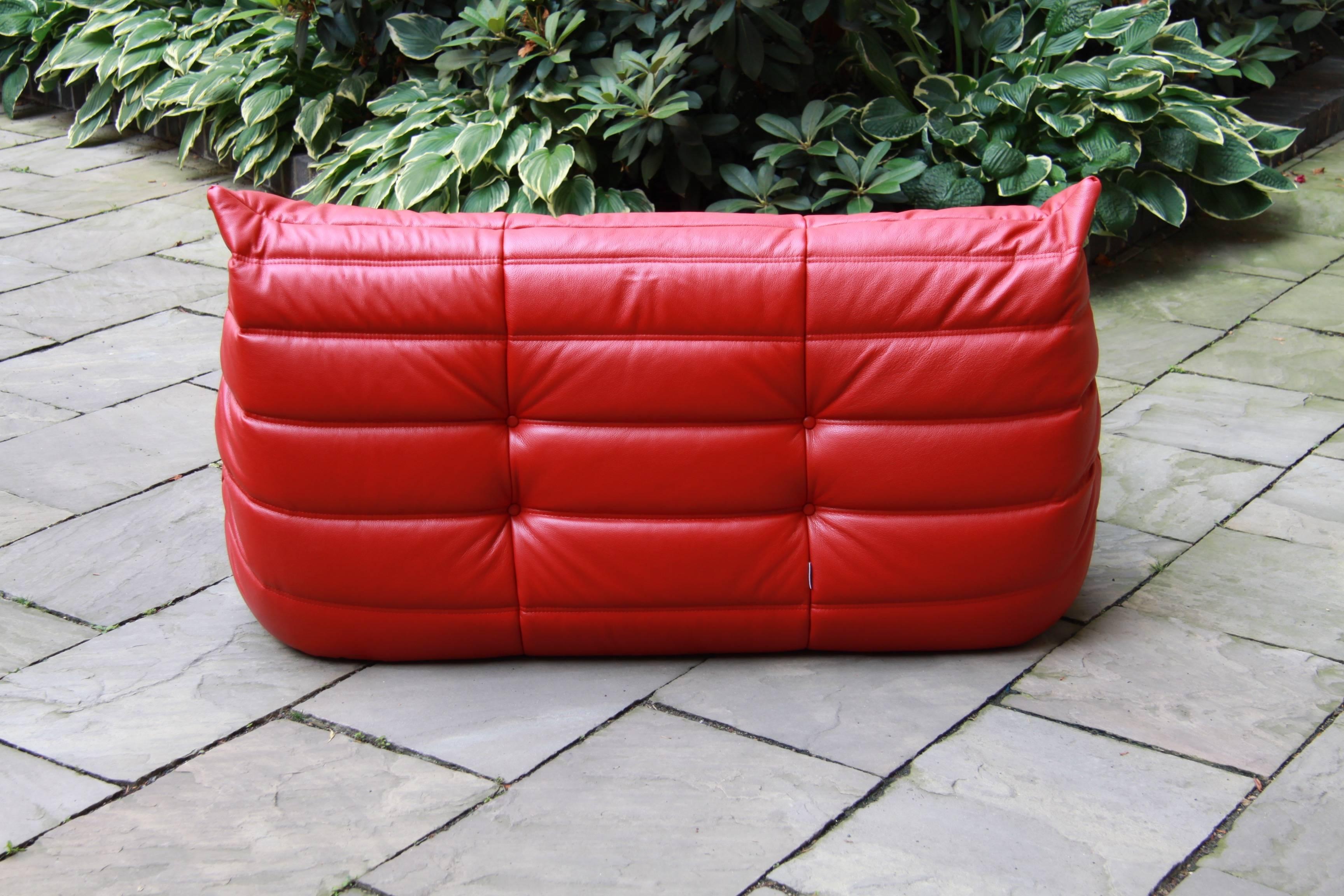 This two-seat Togo sofa (Measures: 70 x 131 x 102 cm) was designed by Michel Ducaroy in the 1970s and was manufactured by Ligne Roset in France. It has been reupholstered in red leather and it features the original Ligne Roset logo at the bottom.