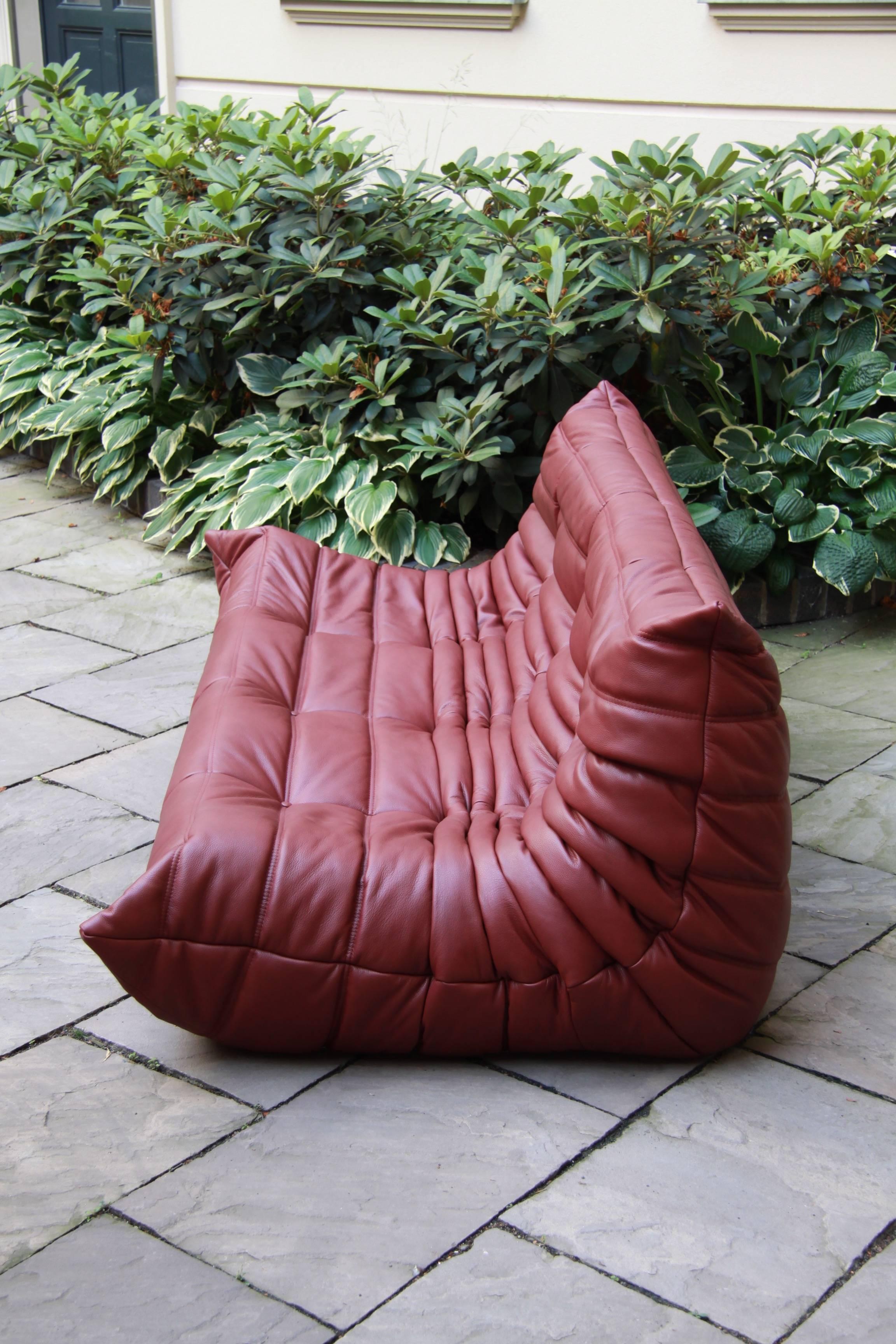 This Togo sofa was designed by Michel Ducaroy in 1974 and was manufactured by Ligne Roset in France. It has been reupholstered in genuine burgundy leather and seats three people. It has the original Ligne Roset logo.