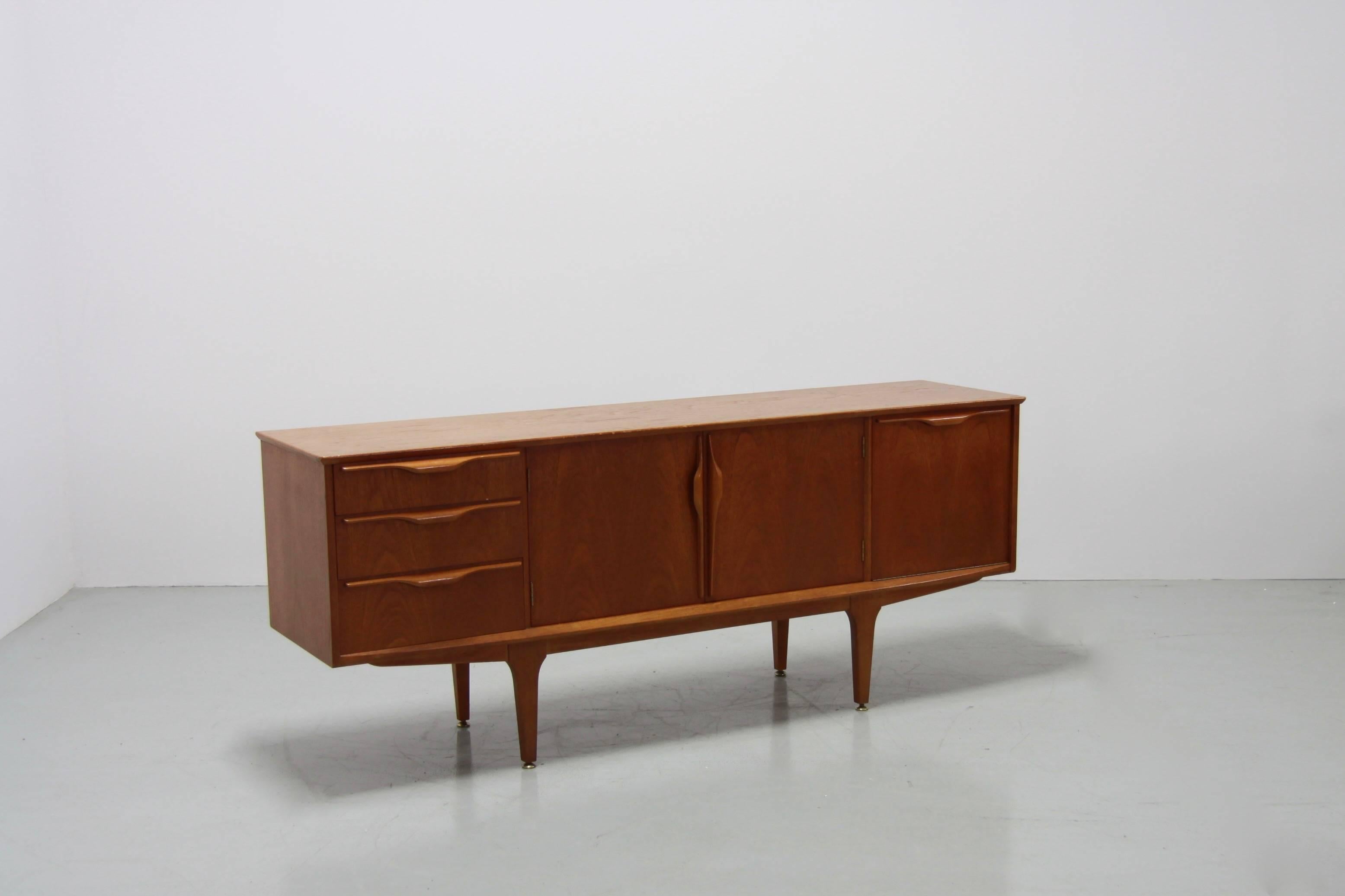 This beautiful classic sideboard was manufactured in 1960s by Jentique in Norfolk, England. It has handcrafted handles and is made from solid teak. The upper drawer is padded with green fabric and the feet are decorated with metal details.