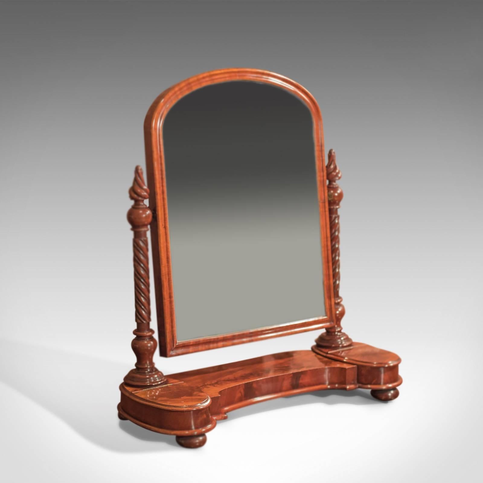 This is an antique, Regency vanity mirror dating to circa 1820.

Raised on squat bun feet, the shaped platform is flanked by a pair of ovular, hinged lid, velvet lined jewelry compartments. The flame mahogany displaying the most wonderful grain