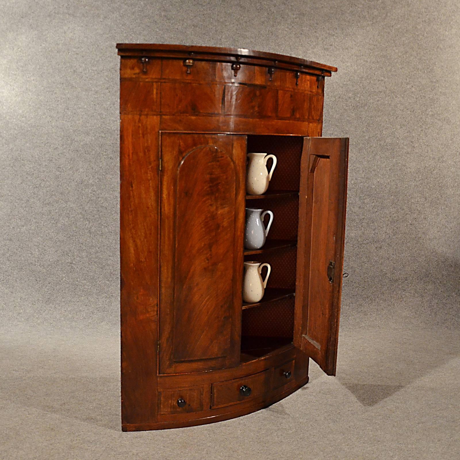 A pleasing English Victorian corner wall cabinet presented in very good antique condition
In stunning flame mahogany veneer
Rising from flush base
Desirable bow front
Central drawer flanked by faux fronts; all with cross-banded edge detail
Twin