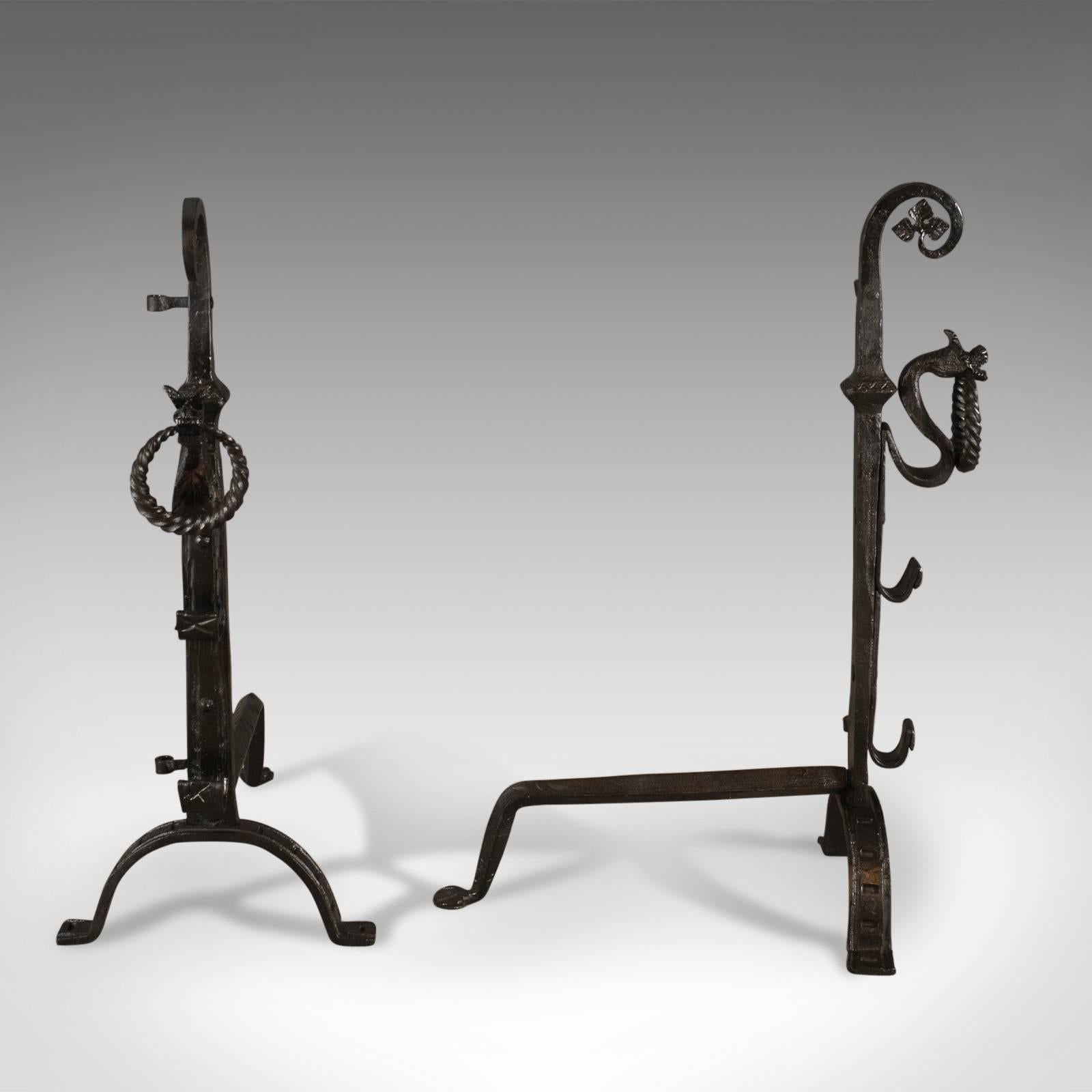 This is a pair of Gothic wrought iron firedogs, medieval revival andirons forged in the late 20th century.

Bold andirons ideal for a large fire basket
Standing upon a tripod with forward arch legs
Medieval revival in taste
Featuring spit