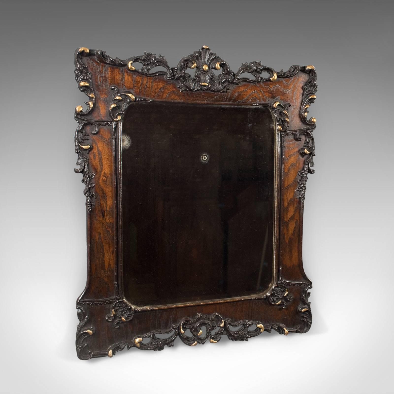 This is an antique wall mirror in an oak frame from the late Victorian period, English, circa 1890.

Attractive grain interest highlighted with the dark stained finish
Pierced mounts of carved 'C' scrolls, shells and foliate swags
Ebonized and