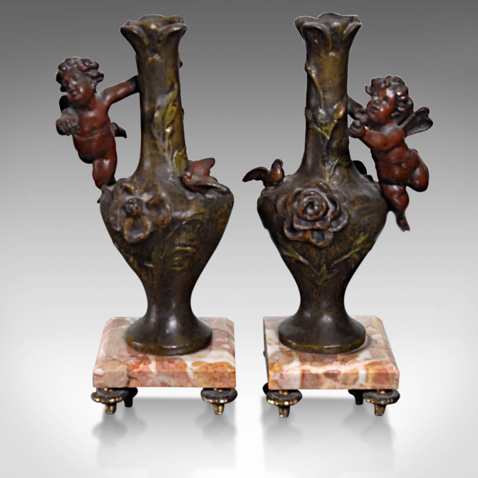 This is an antique pair of candlesticks in the form of cherubs and urns upon marble plinths. Although they could equally well serve as vases for individual flowers when not supporting an elegant candlestick.

Delightful in every aspect, this pair