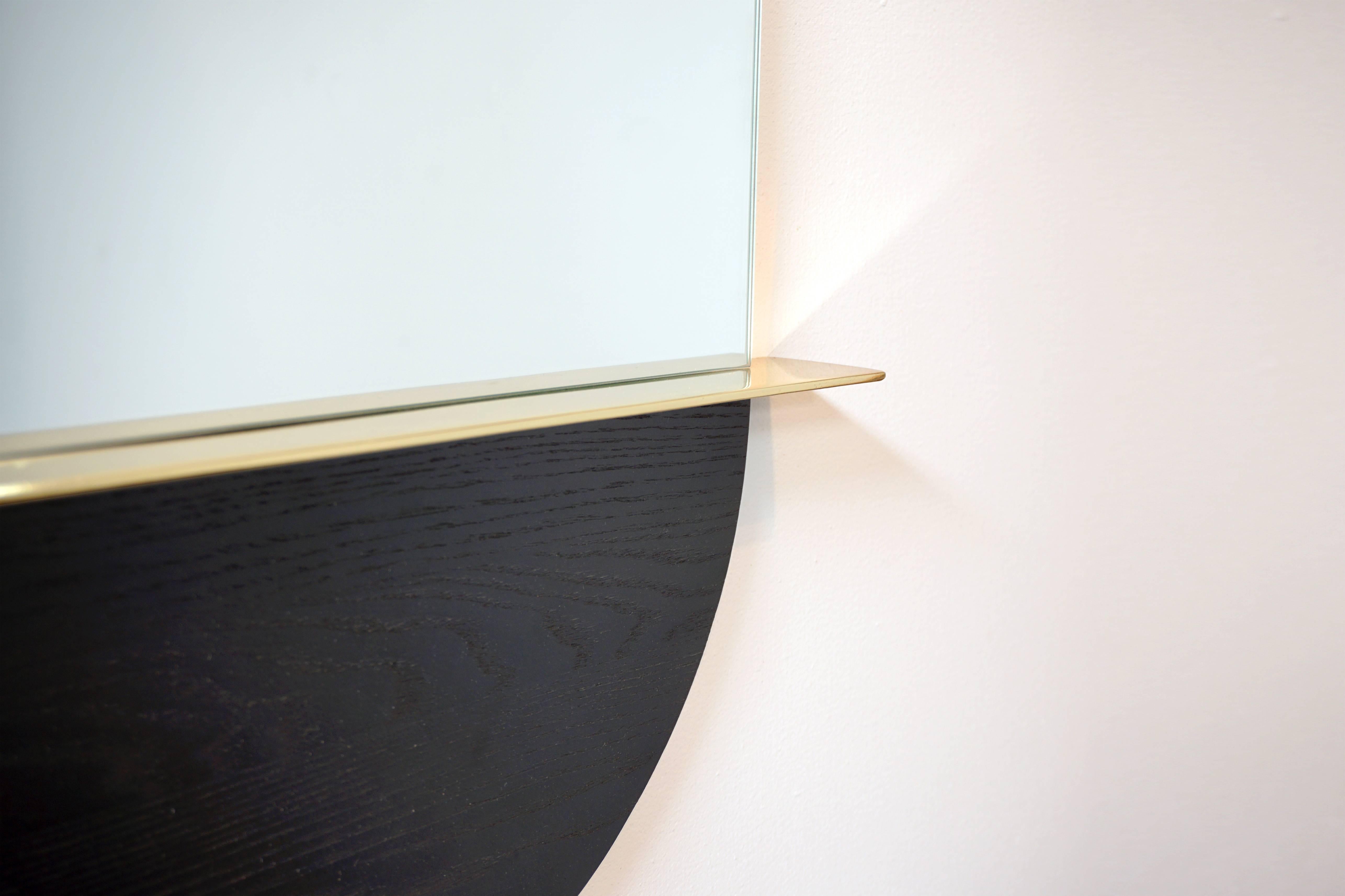 Part blackened ash, brass plated steel and part glass, the Solis Mirror references the horizon, the rising sun, and your reflection among it all. A brass circle stands an inch behind the oblong mirror as if hovering behind. The mirror's glass ends